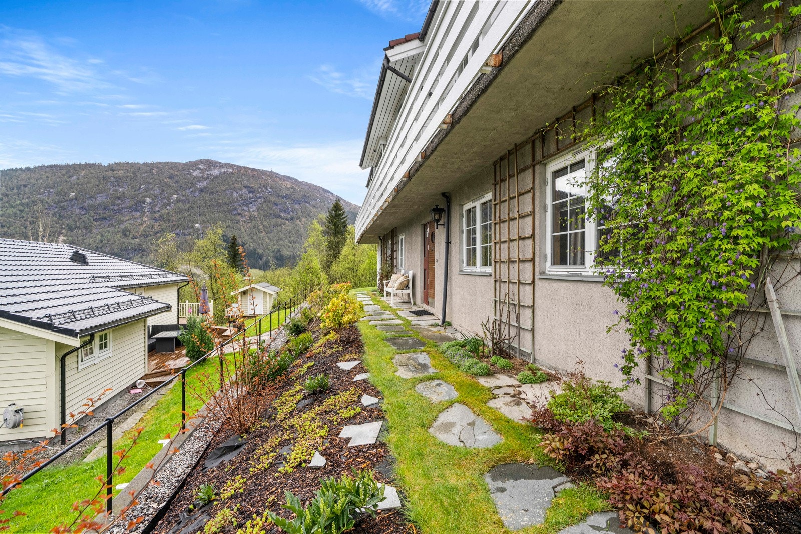 Rundt boligen er det grøntarealer med blomsterbed, plen, hellelagte stier, trapper og utvendig belysning Galleribilde