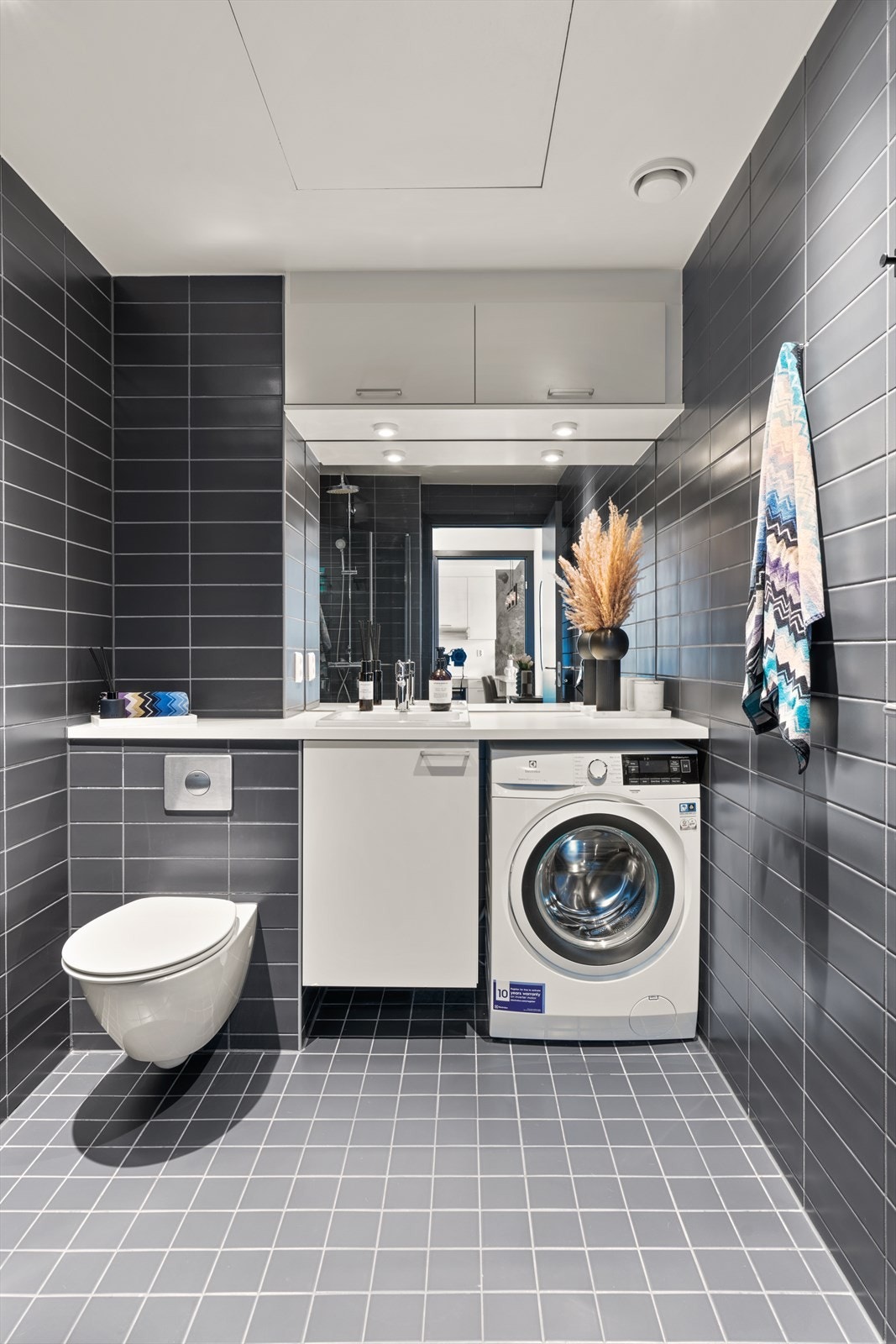 Baderomsinnredningen består av servant, ett-greps blandebatteri, vegghengt wc og dusjhjørne med innfellbare glassdører. Galleribilde