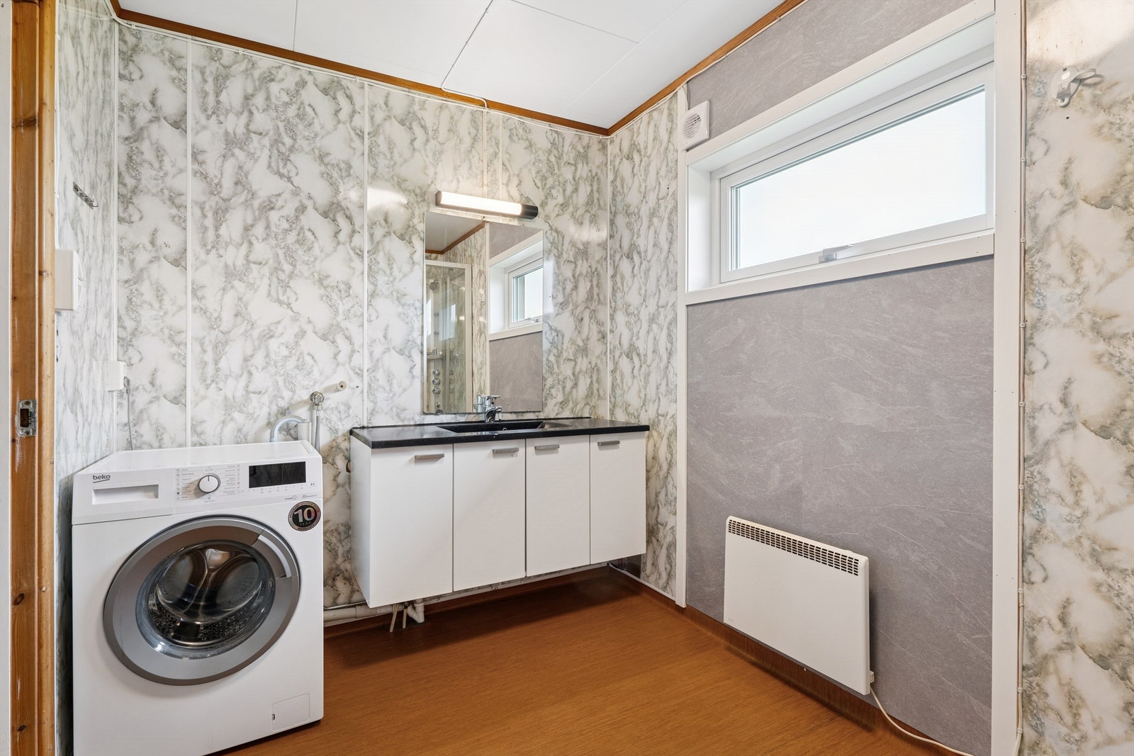 Badet er av eldre årstall og er utstyrt med dusjkabinett, servant med underskap og speil med belysning. Galleribilde