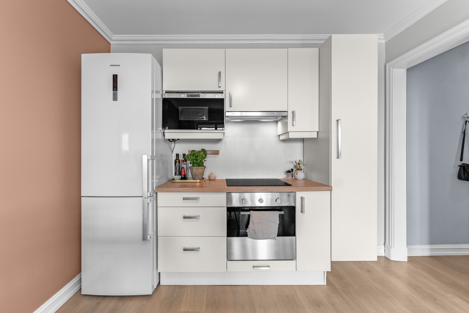 Lyst og funksjonelt kjøkken med hvite fronter, benkeplate og hvitevarer. Galleribilde