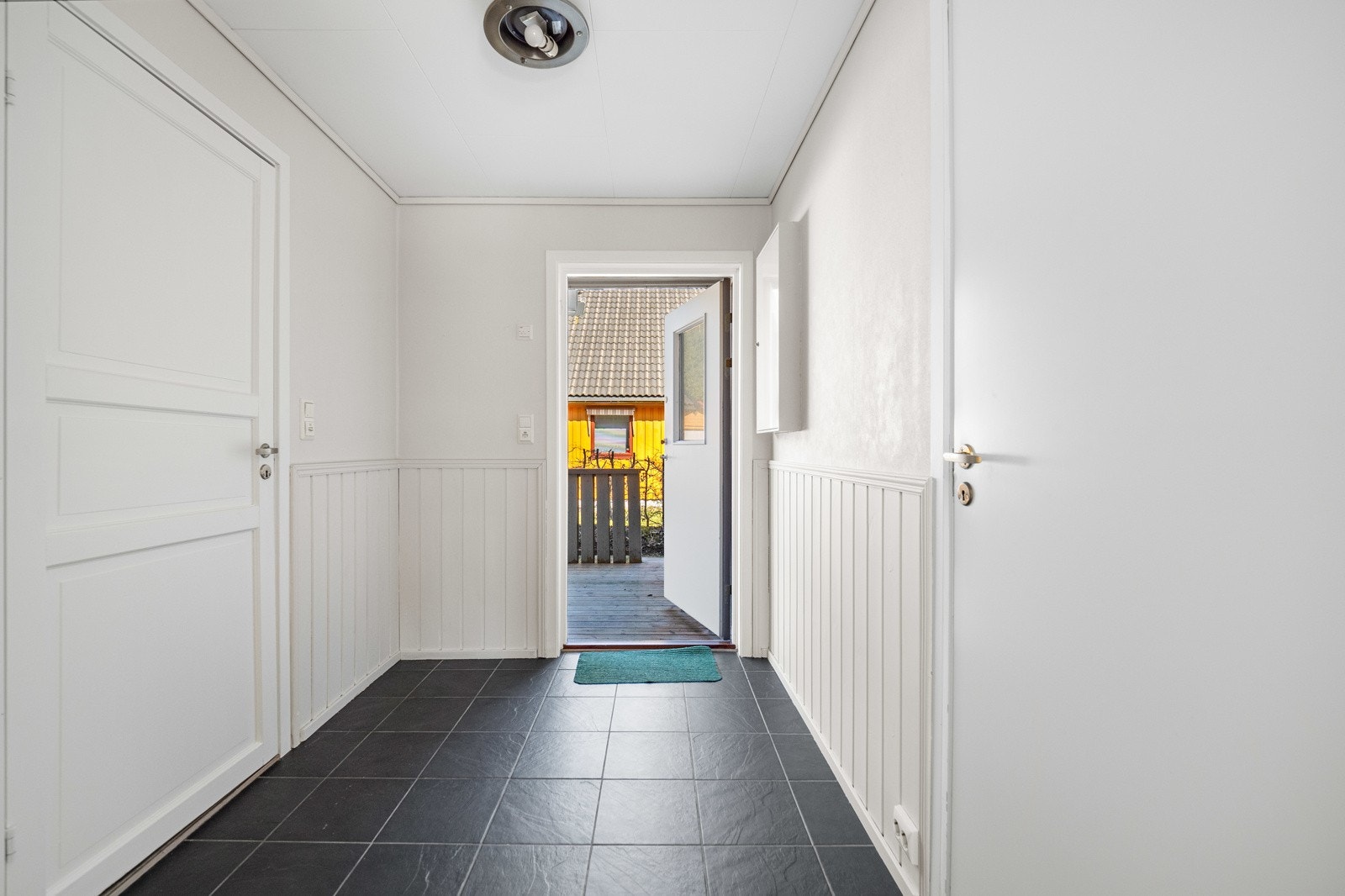 Eneboligen har en flislagt entré med lysmalte vegger, dør med glassfelt inn til stuen og plass til garderobeløsning. Galleribilde