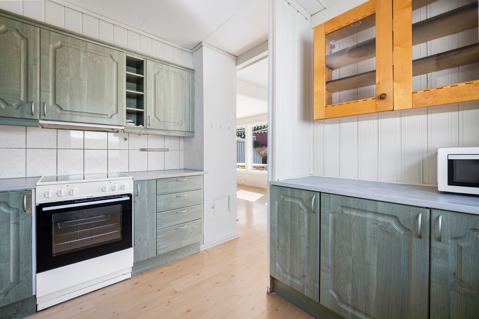 Kjøkken og stue har lysmalte veggflater med panel og brystningspanel, samt et trehvitt laminatgulv. Galleribilde