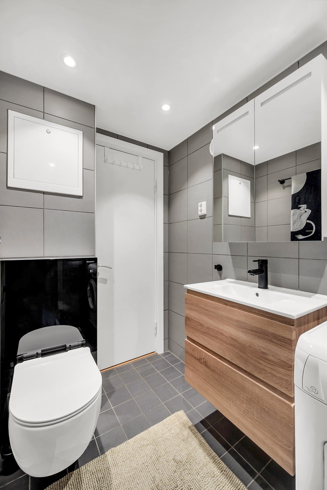 Det er innredet med vegghengt toalett, dusjhjørne med innfellbare glassdører og baderomsinnredning med skuffer, servant nedfelt i innredning og speilskap med belysning. Opplegg for vaskemaskin. Galleribilde