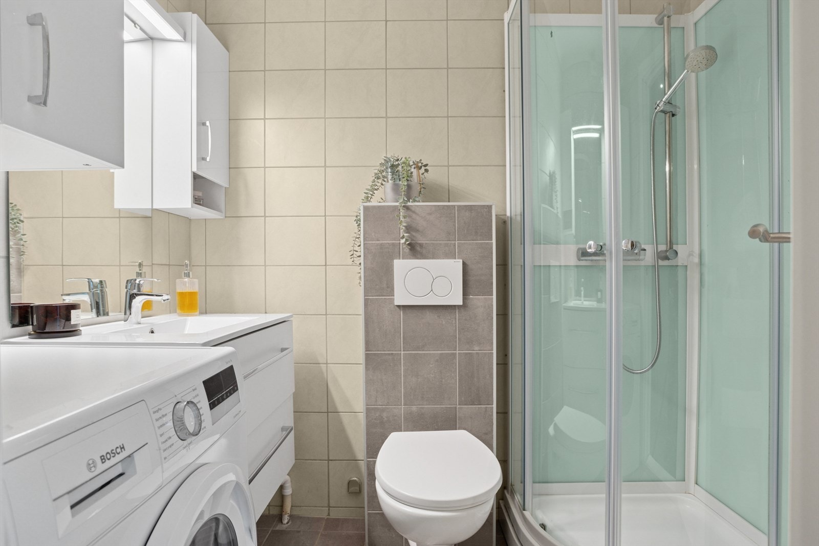 Pent baderom med fliser på både gulv og vegger, samt behagelige varmekabler som gir ekstra komfort. Rommet er utstyrt med moderne servant med innredning, vegghengt toalett, dusjkabinett og opplegg for vaskemaskin. Galleribilde