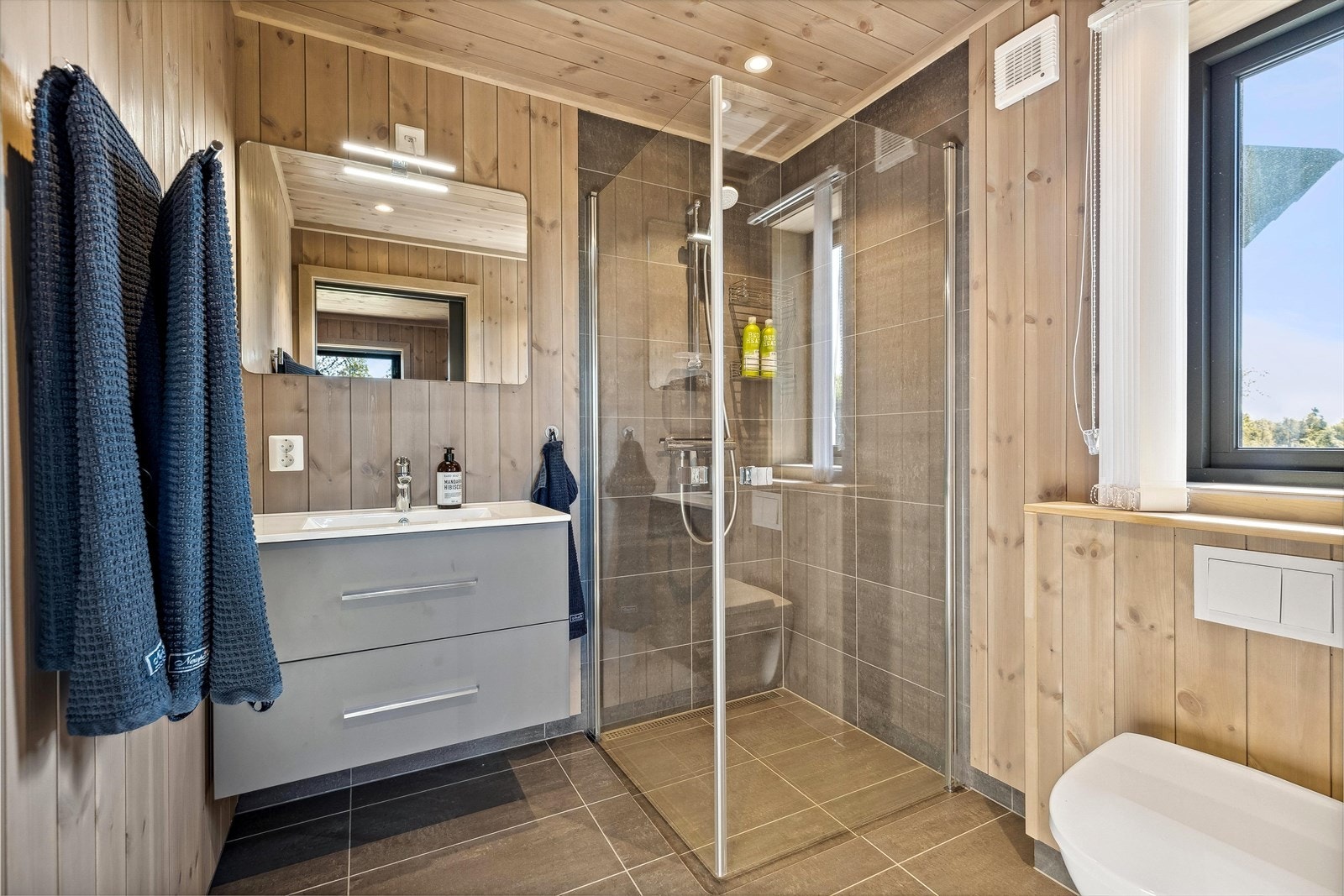 Rommet er innredet med vegghengt toalett, dusjhjørne med glassvegger og innredning med servant. Galleribilde