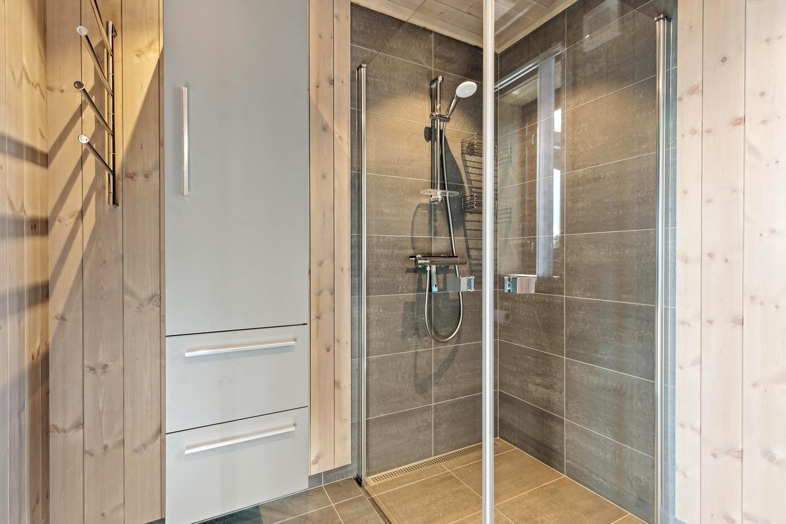 Baderom II har flislagt gulv med varme i og er innredet med vegghengt toalett, dusjhjørne med glassvegger, innredning med servant og veggskap. Galleribilde