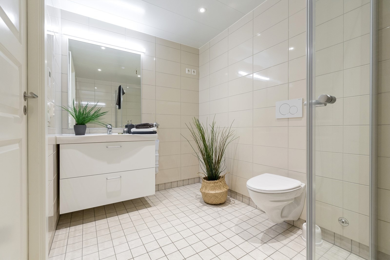 Badet har innredning med nedfelt servant med skuffeseksjon, veggmontert toalett, dusjhjørne og opplegg for vaskemaskin. Galleribilde