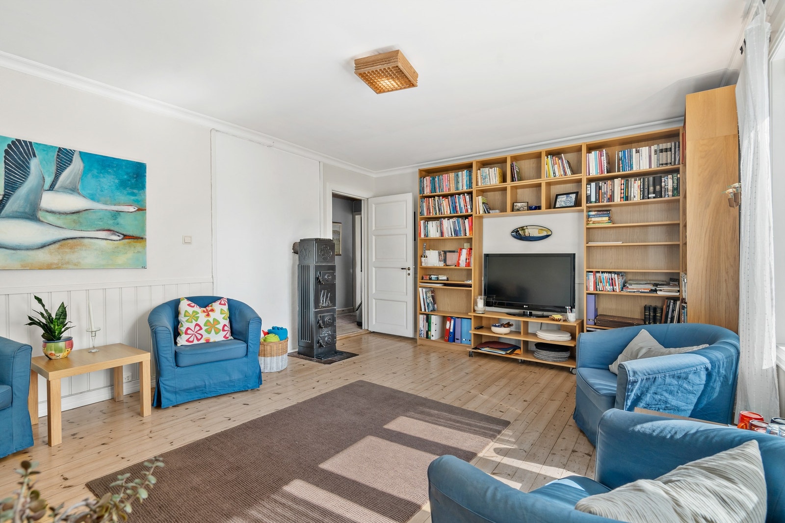 Meget romslig oppholdsrom med ovn og tregulv med lyse overflater Galleribilde