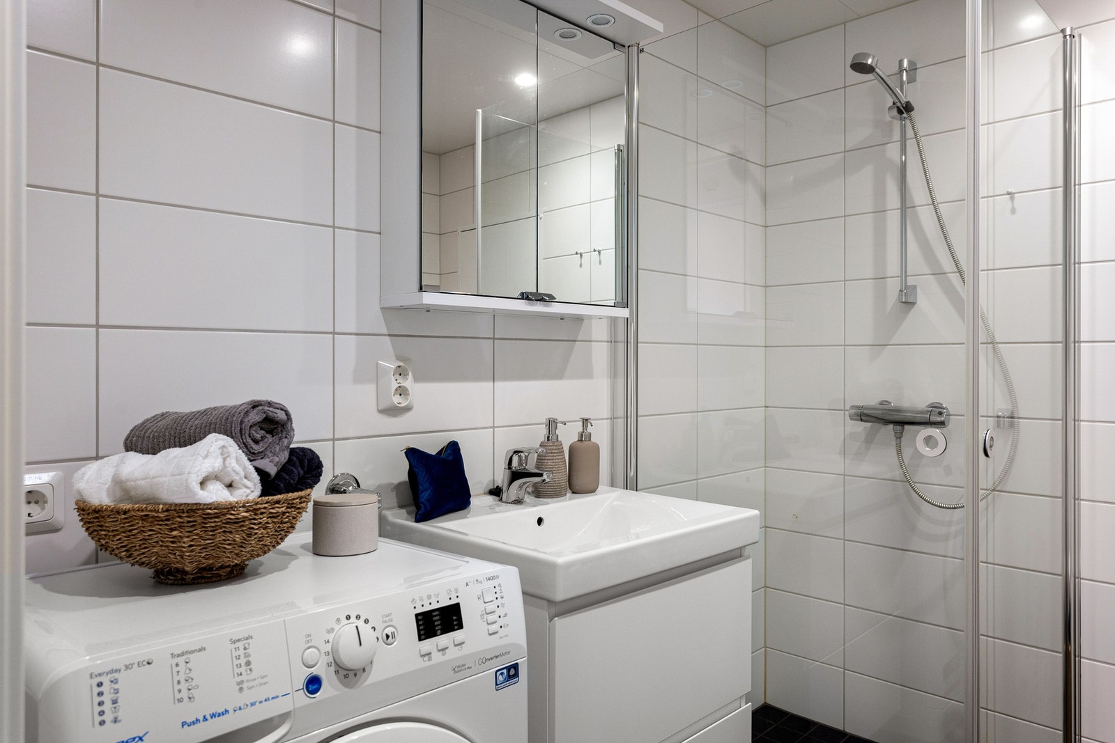 Videre har badet et vegghengt toalett, opplegg for vaskemaskin og et dusjhjørne med innfellbare glassdører. Galleribilde