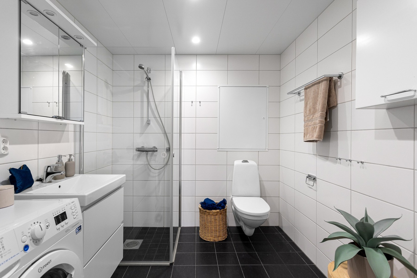 Leilighetens bad fremstår som velholdt og pent, med hvite fliser på veggene, downlights i himlingen og koksgrå fliser på gulv med gulvvarme. Galleribilde