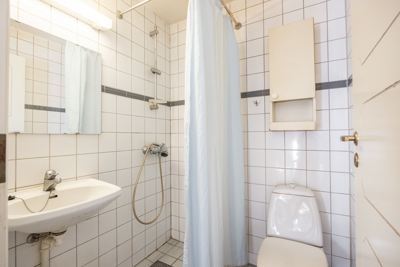 Eldre bad med innredning bestående av enkel servant, WC og dusjhjørne Galleribilde