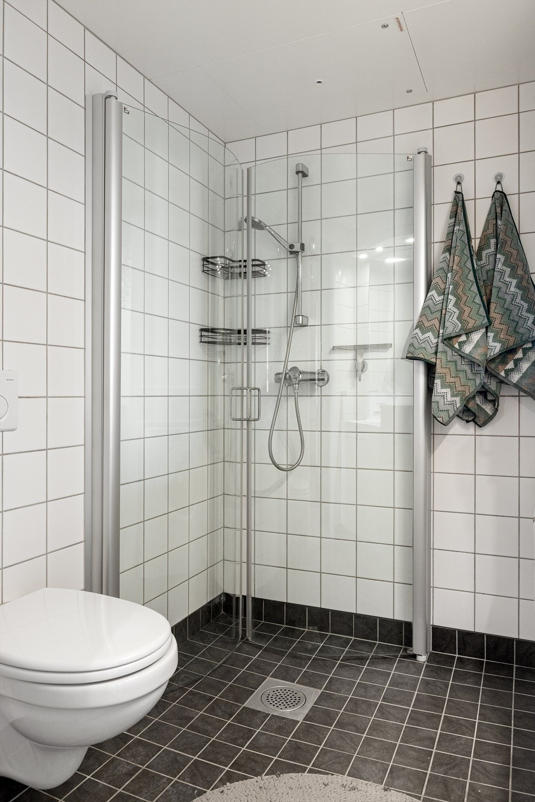 Badet er fra 2008 og består av vegghengt toalett, et romslig dusjhjørne med innfellbare glassdører, en servant med underskap og speil med integrert belysning, samt opplegg for vaskemaskin. Ventilasjon er via mekanisk avtrekk. Galleribilde