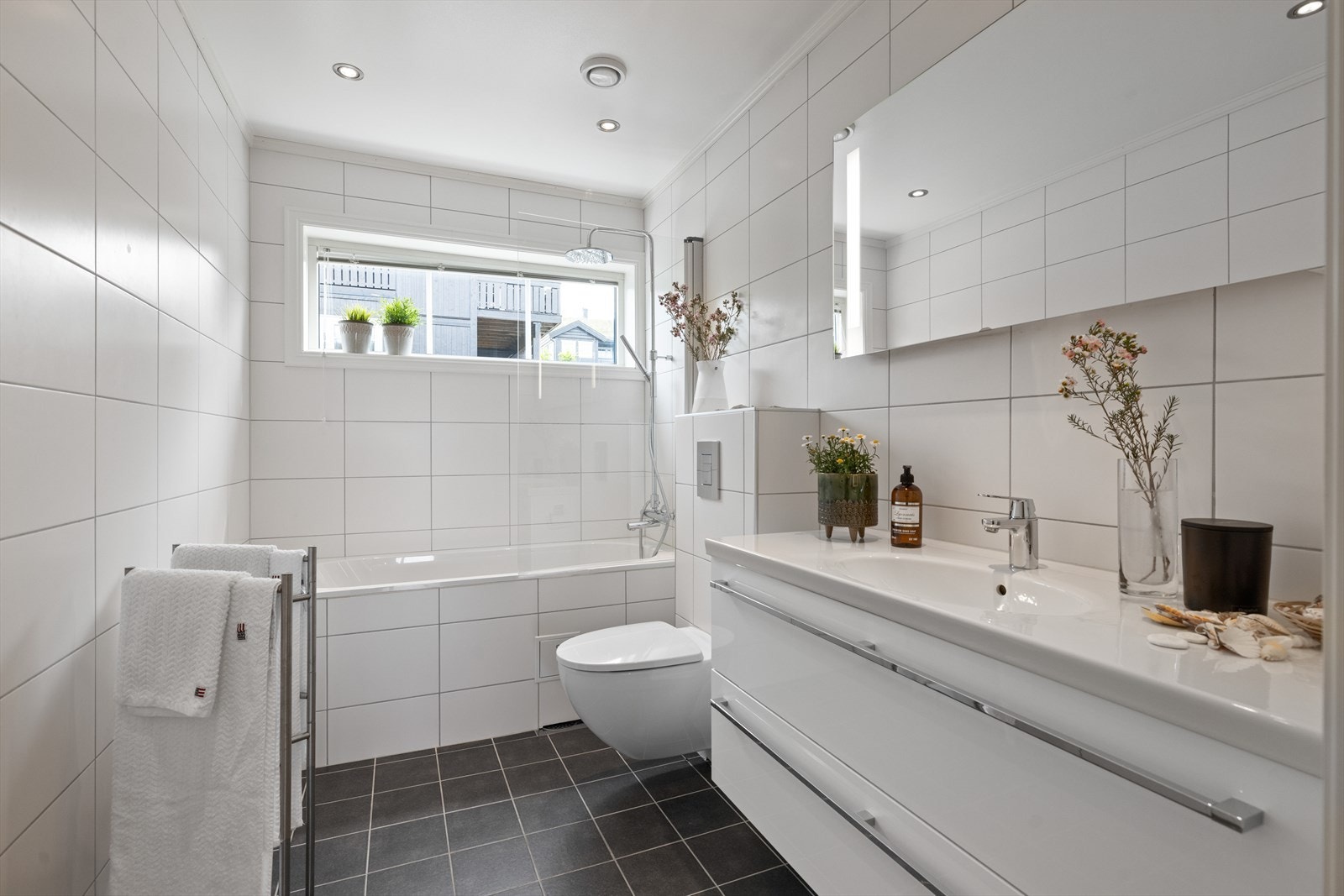 Pent flislagt bad/wc med varmekabler, downlights, speil med belysning, avtrekk. Innmurt badekar med innfellbar glassdør, vegghengt toalett og servant med innredning Galleribilde