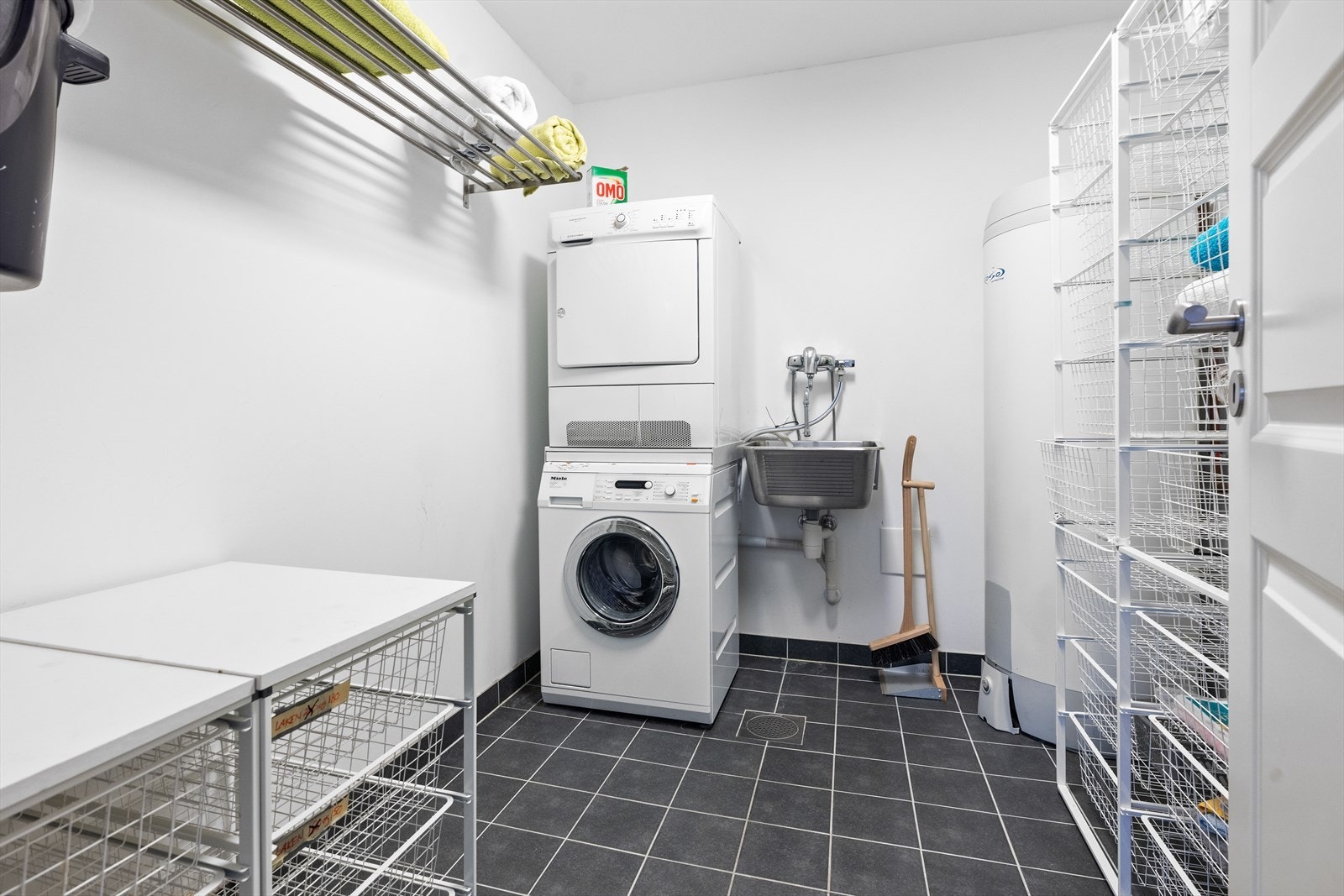 Praktisk vaskerom med flislagt gulv og varmekabler, sokkelflis, malte flater på vegger. Utslagskum, varmtvannsbereder, sentralstøvsuger, opplegg for vaskemaskin og tørketrommel Galleribilde