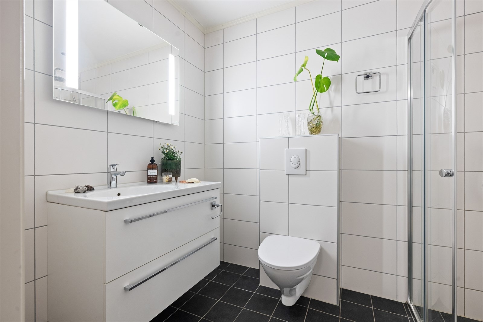 Flislagt bad/wc i underetasje. Varmekabler under fliser, downlights, speil med belysning, skap. Servant med innredning, dusj med innfellbare glassdører og vegghengt toalett Galleribilde