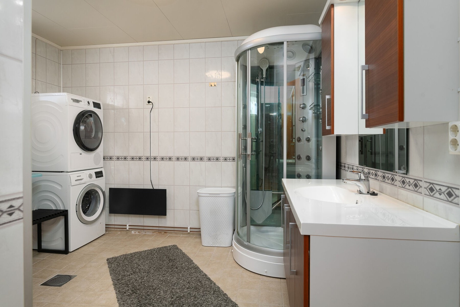 Bad/vaskerom i underetasje med servant på innredning, dusjkabinett og opplegg for vaskemaskin Galleribilde