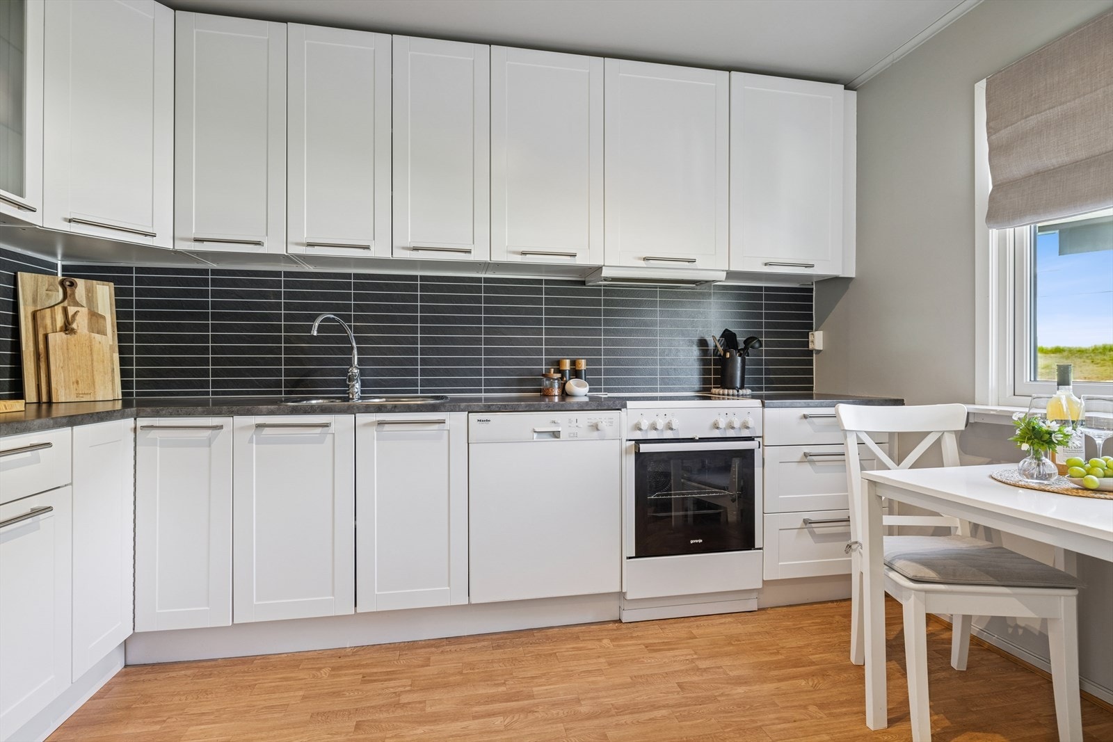 Kjøkkeninnredning i vinkel fra 2000-tall. Hvite, slette, fabrikkmalte MDF-fronter med ett speil på overskap og underskap, samt skuffer. Ett dobbelt overskap med frostet glass. Galleribilde