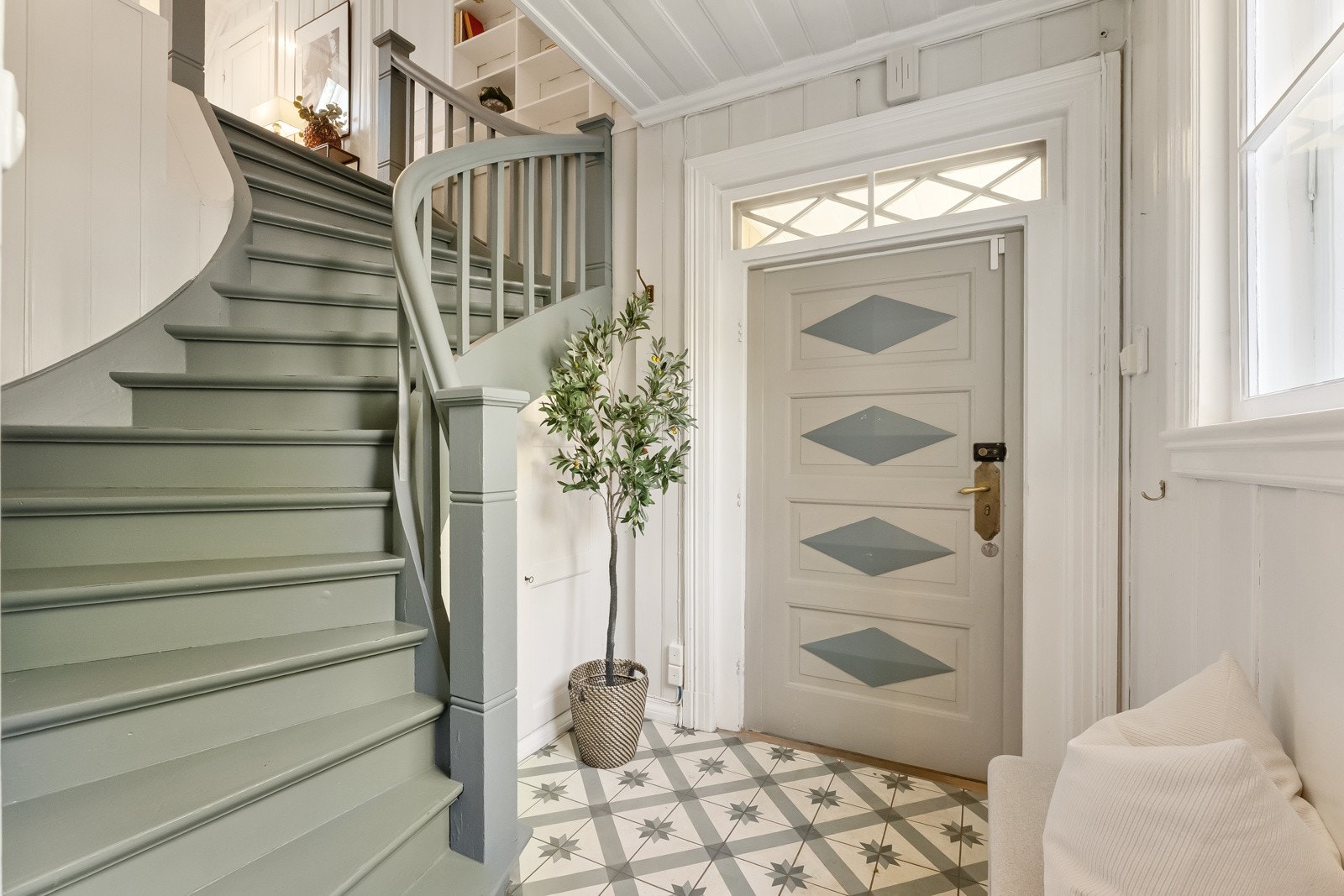 Trappen og detaljer på ytterdøren er malt i en klassisk blåtone, à la Gustaviansk blå, veggene er i hvitmalt panel og gulvet har mønsterfliser i historisk design. Galleribilde