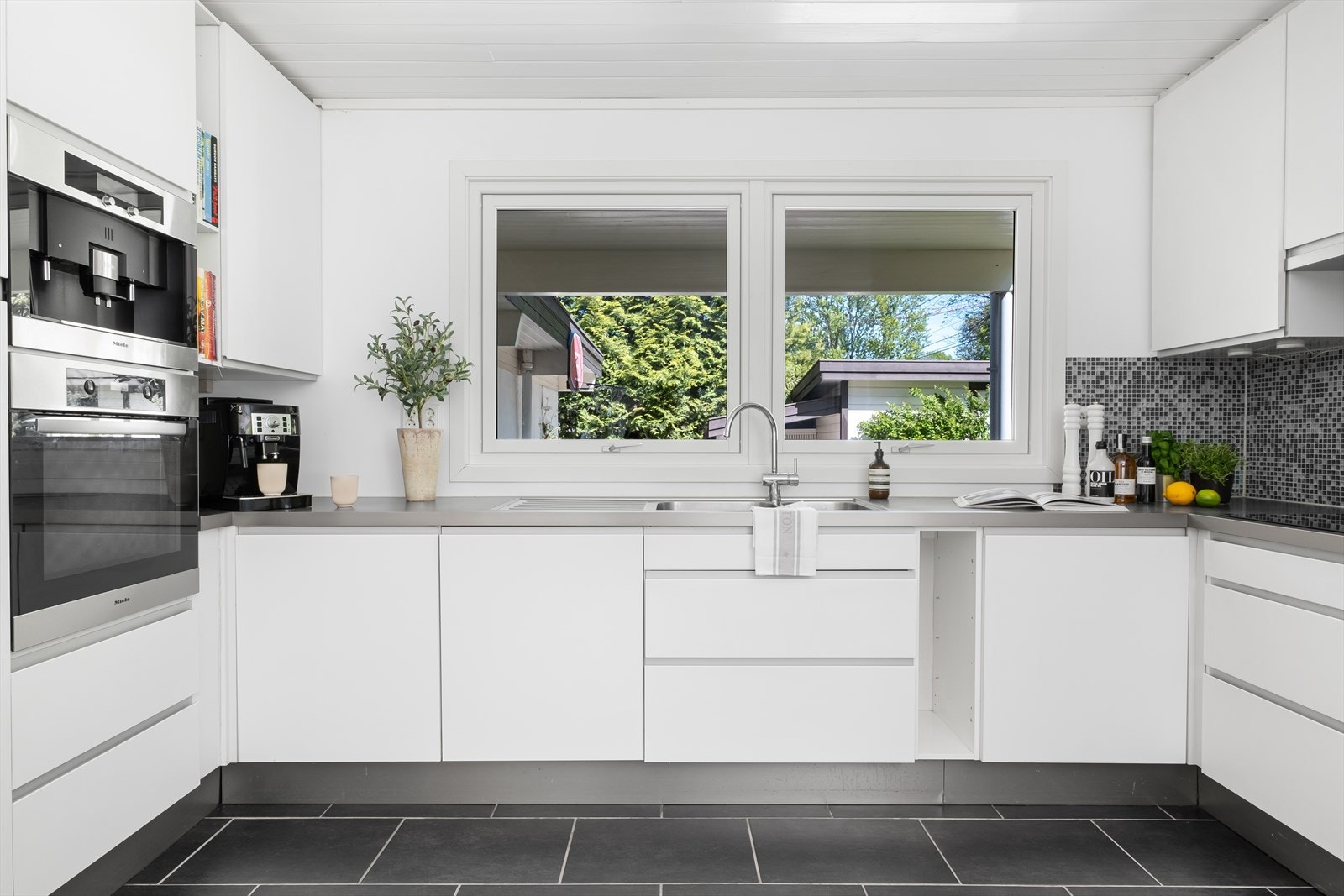 Kjøkkeninnredning med laminerte benkeplater, slette skapfronter, flislagt backsplash og ventilator med utkast til friluft. Galleribilde