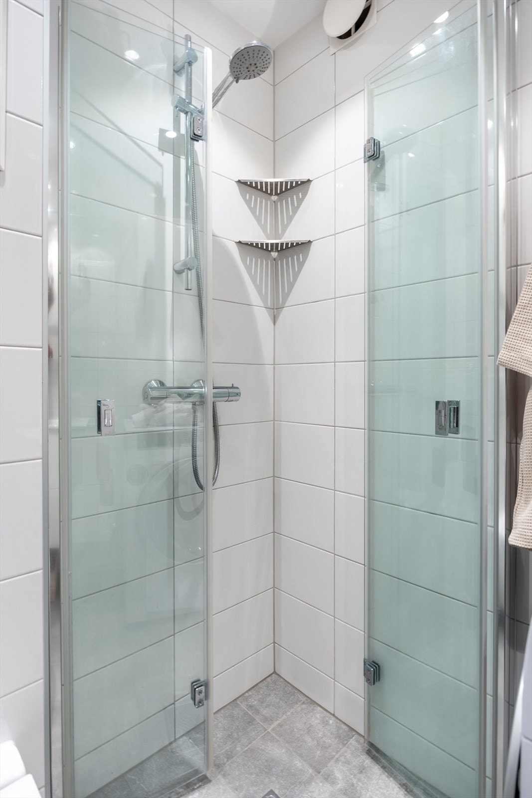 Baderommet er utstyrt med veggfestet toalett, dusj på gulv med dører i herdet glass, servant med innredning og overskap med speilfronter Galleribilde