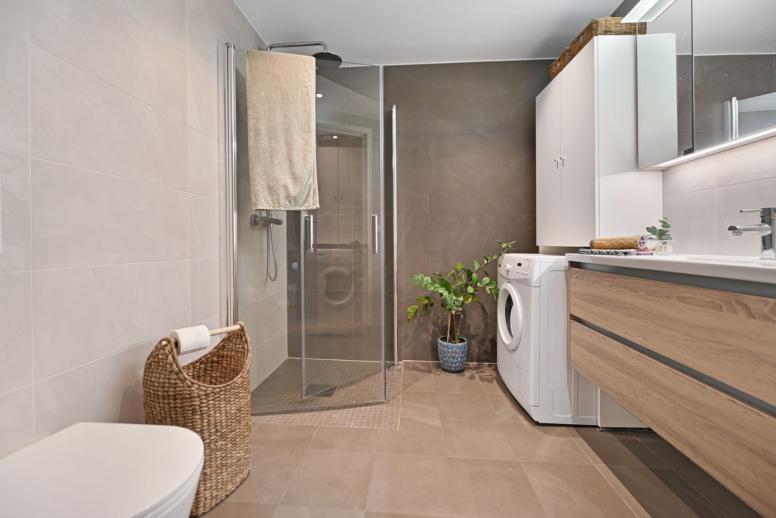 Badet er innredet med nedfelt servant, veggfestet toalett, dusjhjørne og opplegg for vaskemaskin. Galleribilde