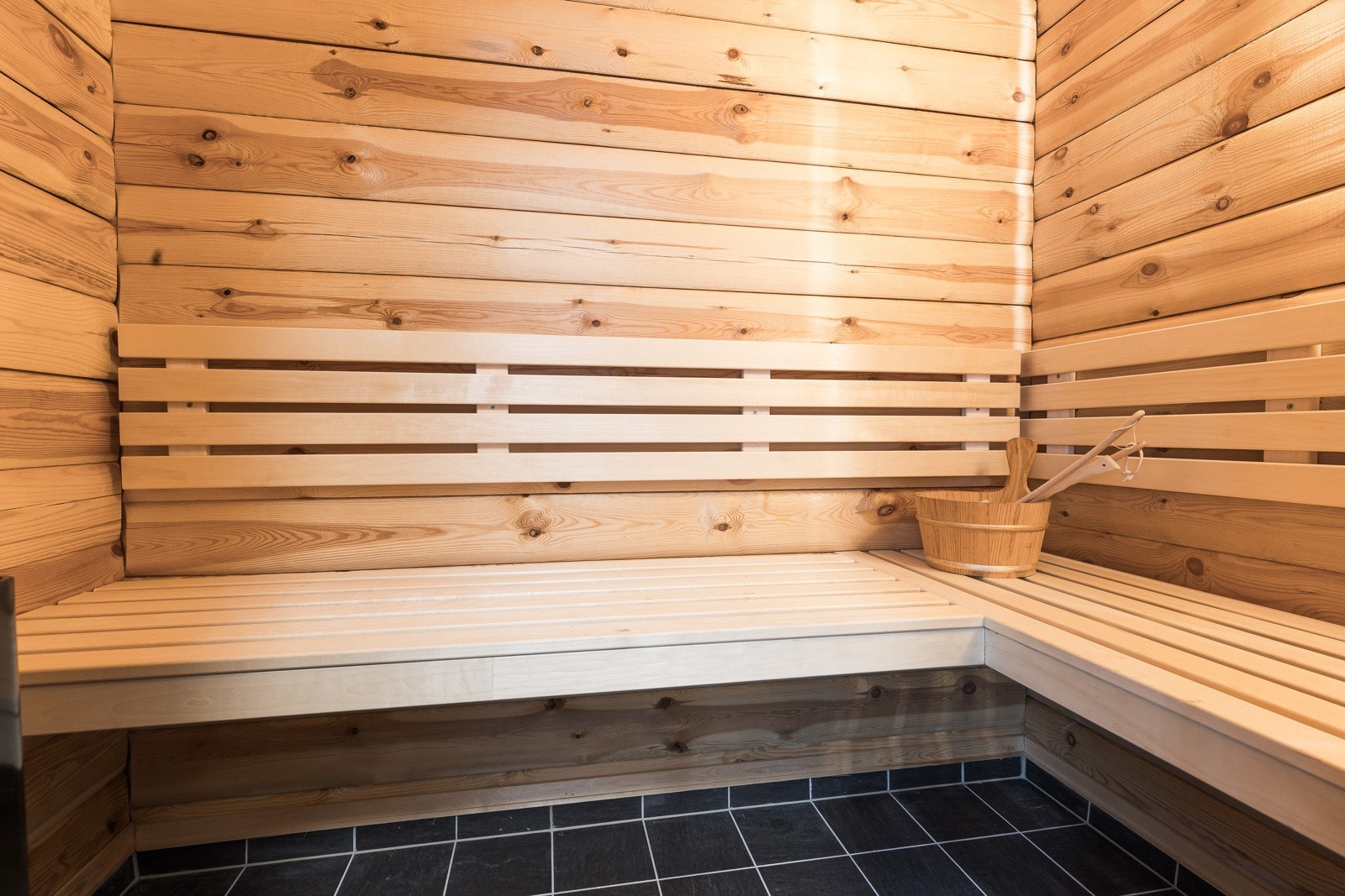 Badet har glassdør inn til en badstue med flislagt gulv, badstueovn og plassbygde trebenker. Galleribilde