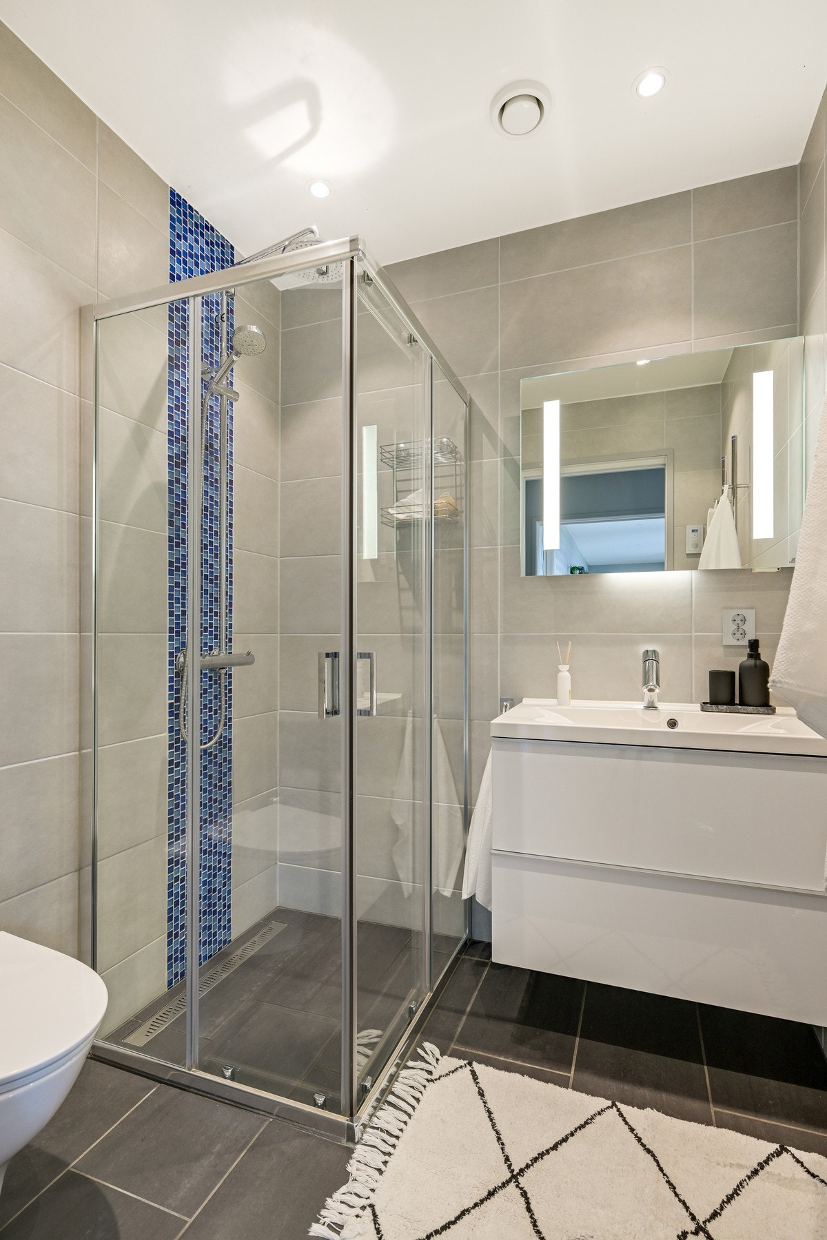 Dusjhjørnet på det andre badet er utstyrt med regnfallsdusj og skyvedører. Baderomsinnredningen er levert av Foss bad, bestående av et speil med integrert belysning og en servant med hvite skuffer. Galleribilde