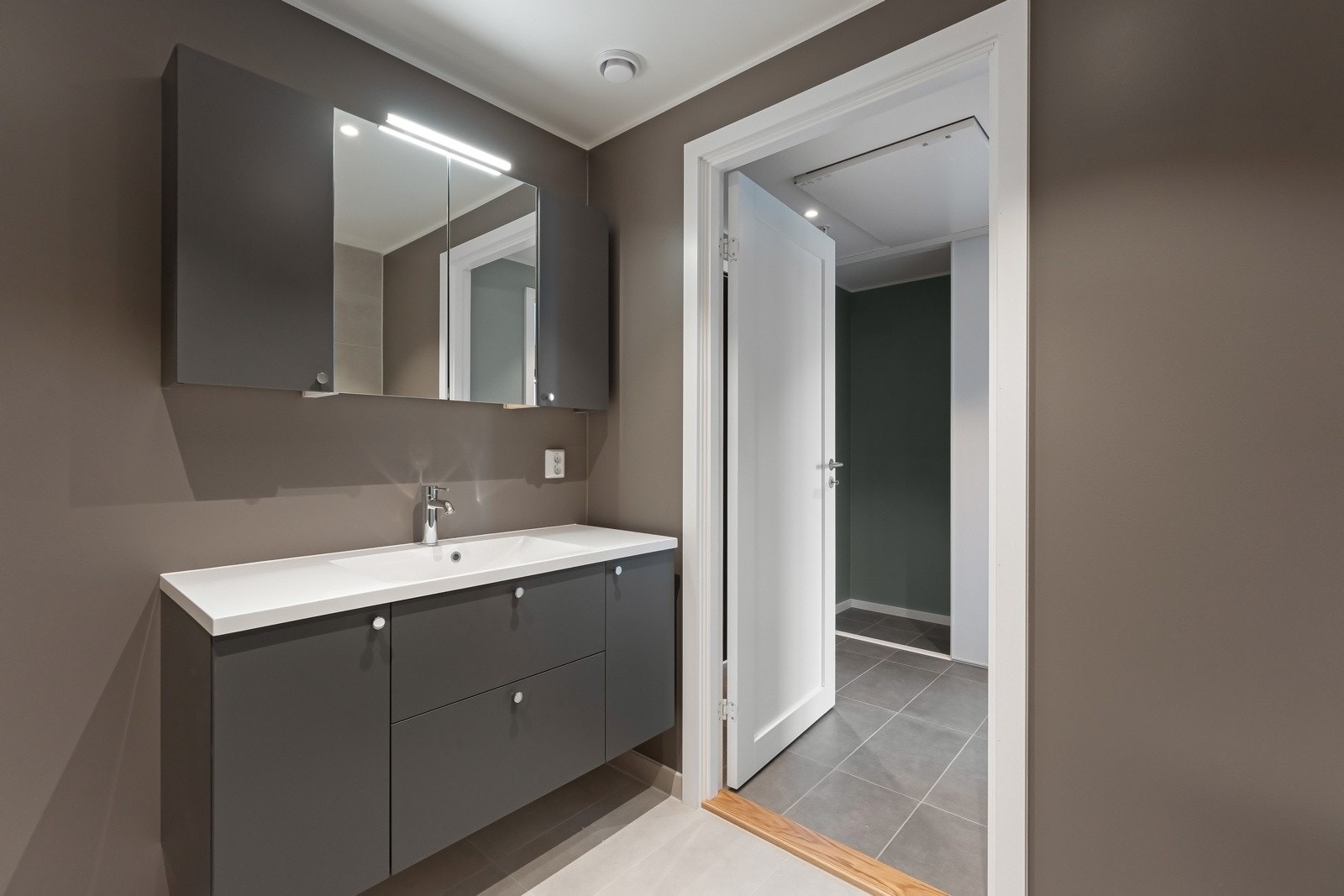 Badet har innredning med nedfelt servant, veggmontert toalett, dusjhjørne og opplegg for vaskemaskin. Galleribilde