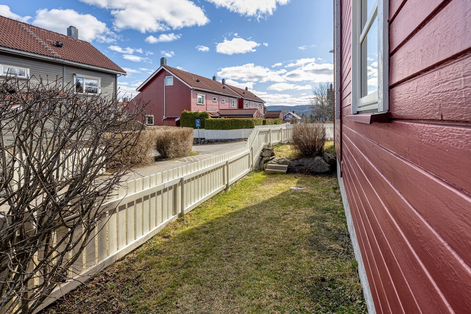 Det er mulig å gå rundt huset til hagen. Her er det plen og malte gjerder Galleribilde
