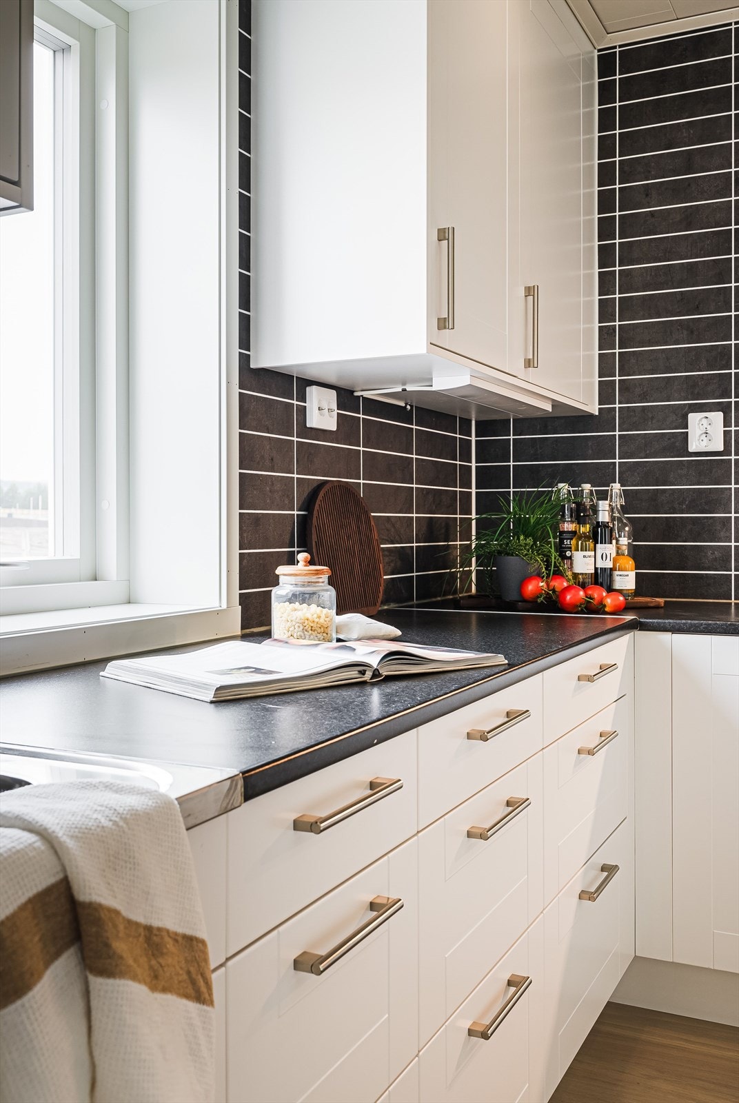 Innredningen har hvite profilerte fronter og laminert benkeplate med nedfelt oppvaskkum. Praktisk med flisimitasjonsplater i benkeryggen og belysning under overskap. Galleribilde