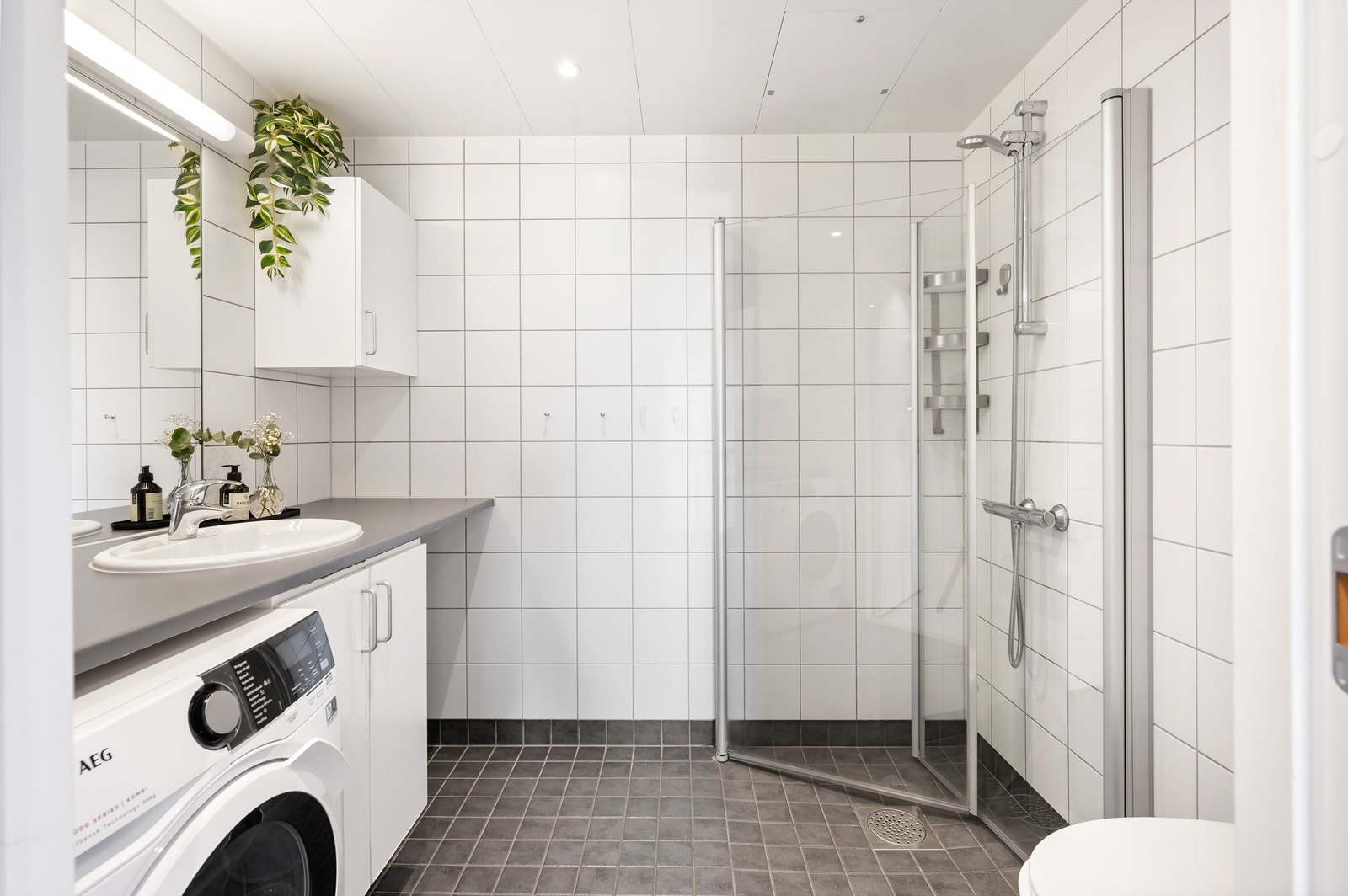 Lyst og pent flislagt baderom med downlights i himlingen og behagelig gulvvarme. Innredningen består av vegghengt servantskap med dører, heldekkende benkeplate av laminat med nedfelt servant og ett-greps armatur. Galleribilde