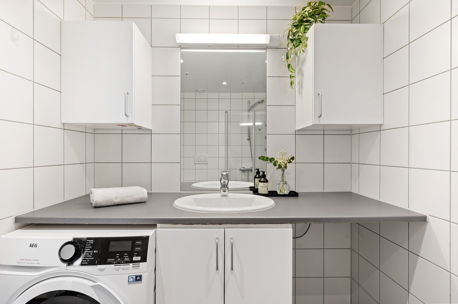 Det er montert speil og veggskap over servant/benk. Videre har badet dusj på gulv med innfellbare glassdører og vegghengt toalett. Opplegg for vaskemaskin/tørketrommel under benk. Avtrekksventil i himling. Galleribilde