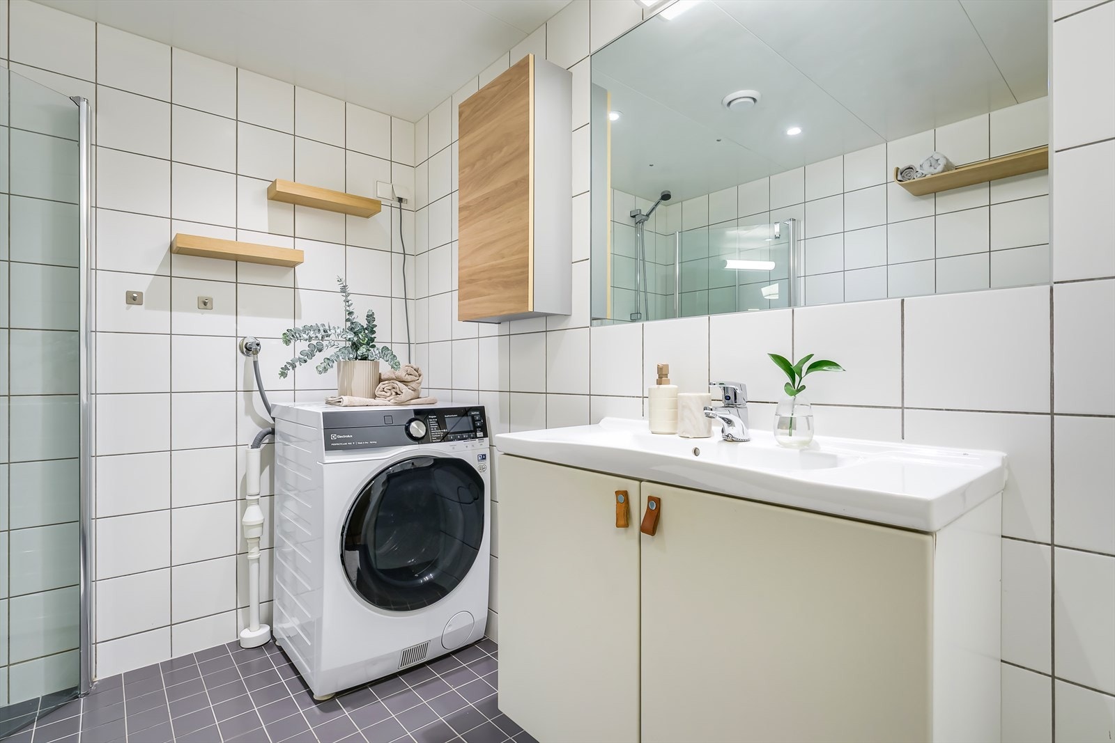 Badet er innredet med dusjhjørne bak svingbare glassvegger, heldekkende servant på benkeskap, vegghengt toalett og speil med lys. Det er opplegg for vaskemaskin. Galleribilde