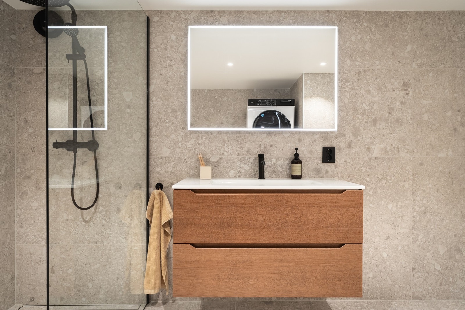 Badet er innredet med dusj m/glassvegg, vegghengt toalett, opplegg for vaskemaskin og baderomsinnredning. Galleribilde