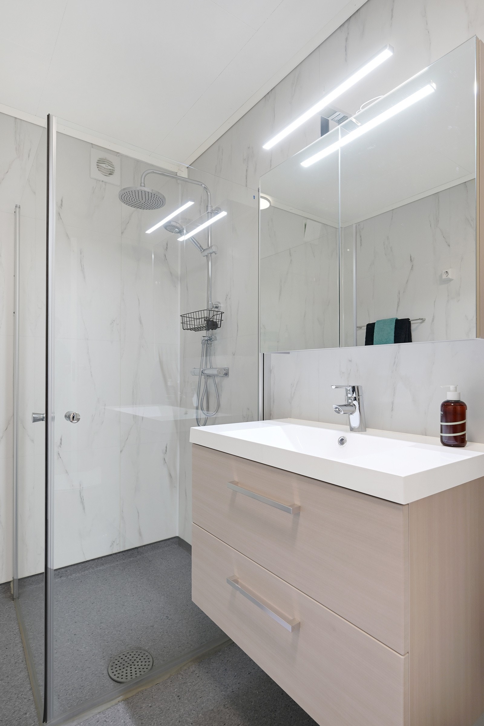 Badet er innredet med praktiske dusjvegger, klosett, pen baderomsinnredning og opplegg for vaskemaskin. Galleribilde