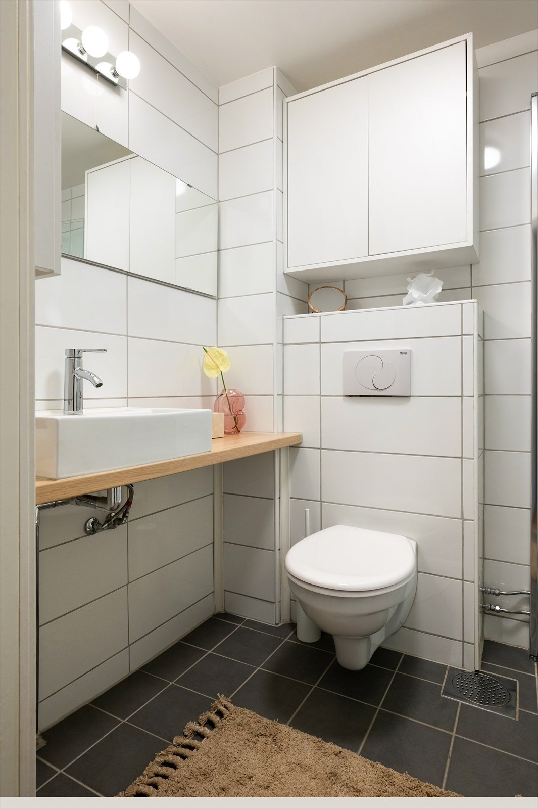 Badet har heldekkende servant på underskap, speil med belysning, vegghengt toalett og dusj med herdet glassdører. Galleribilde