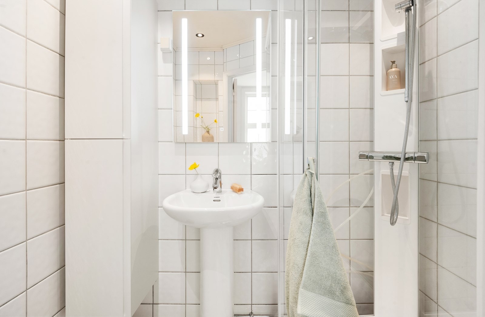 Lyst og fint bad med dusjkabinett og praktisk høyskap til oppbevaring Galleribilde