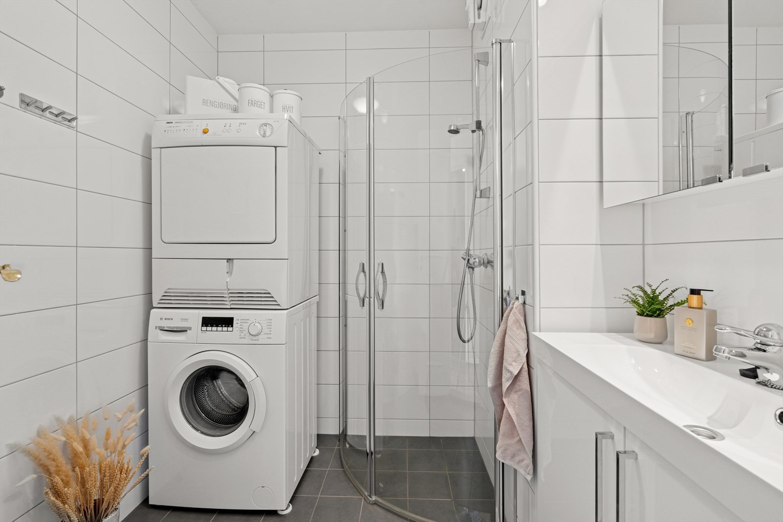 Lyst delikat bad med flislagte overflater. Dusjhjørne og opplegg for vaskemaskin/tørketrommel. Galleribilde