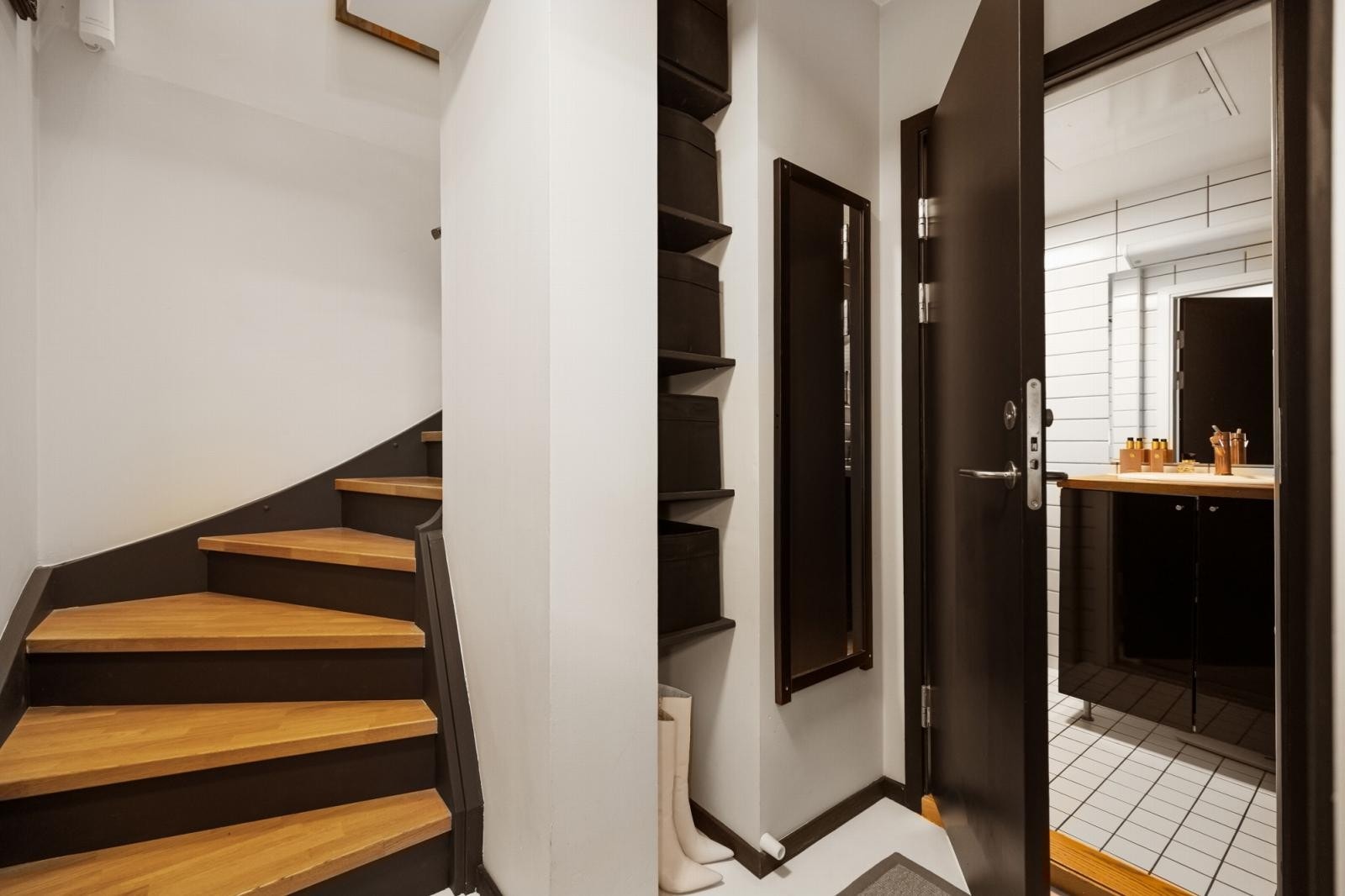 Via leilighetens trapperom tar man turen ned til leilighetens øvrige rom. Her er det laget en plassbygd hylleløsning for ekstra oppbevaring. Galleribilde