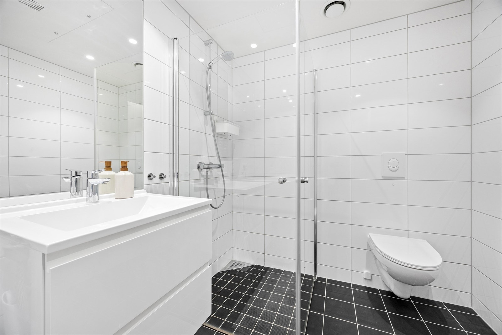 Romslig helfliset bad med nedsenket himling med downlights. Vegghengt servantinnredning med skuffer. Ovenpåliggende servant med ett-greps armatur. Galleribilde
