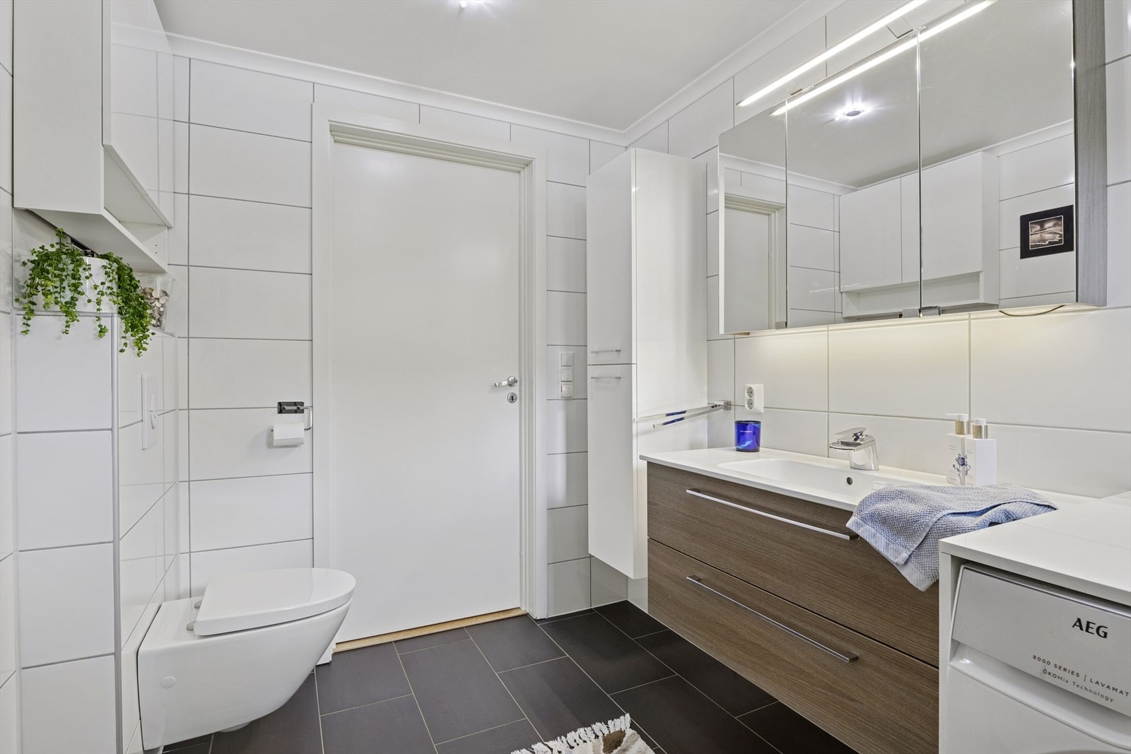 Rommet inneholder innredning med servant, vegghengt wc, dusj med vegger og opplegg for vaskemaskin. Galleribilde