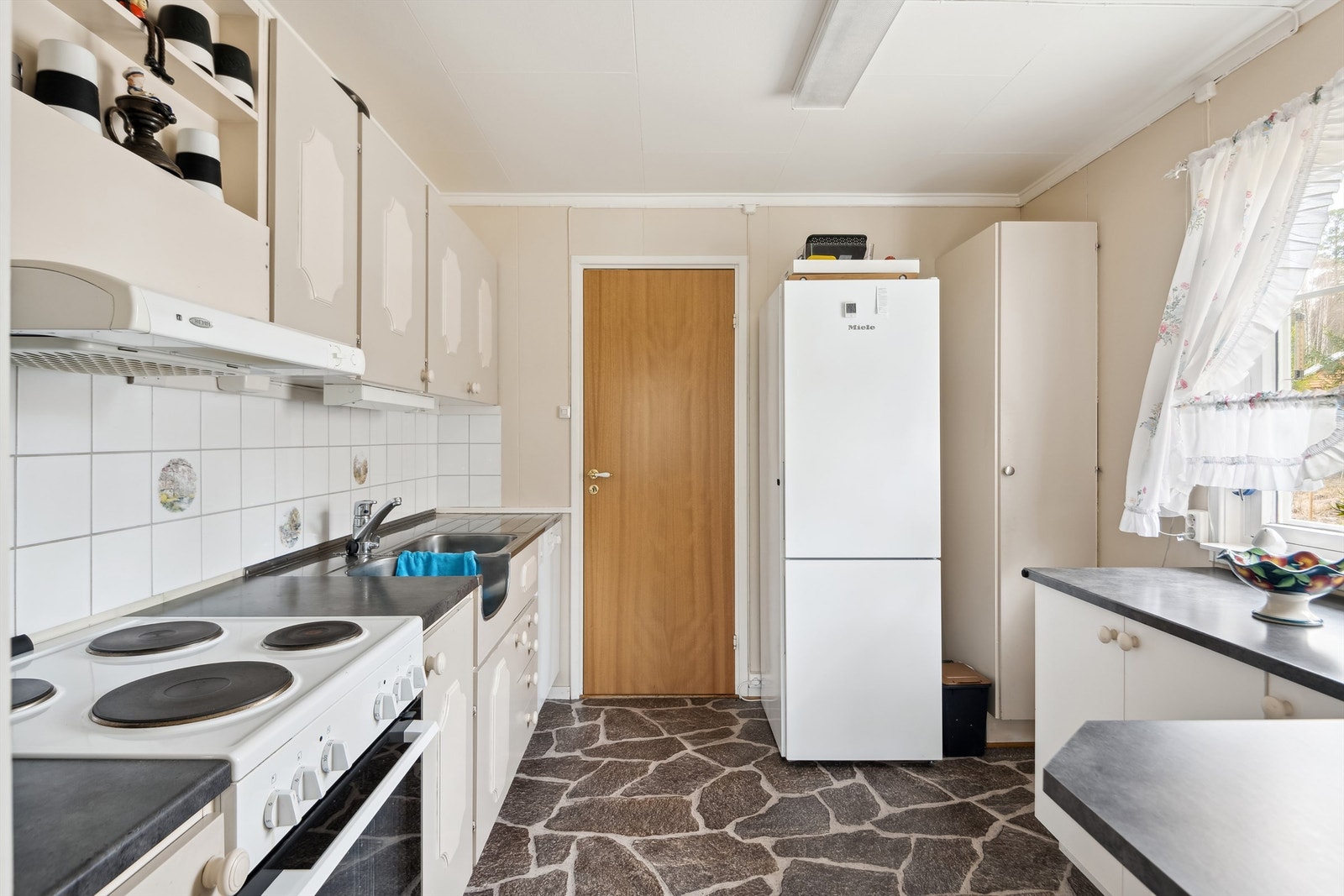 Kjøkkeninnredning av variert alder med malte, laminerte fronter og laminerte skrog og benkeplater. Praktisk benkebeslag med oppvaskkum og utslagsvask. Galleribilde