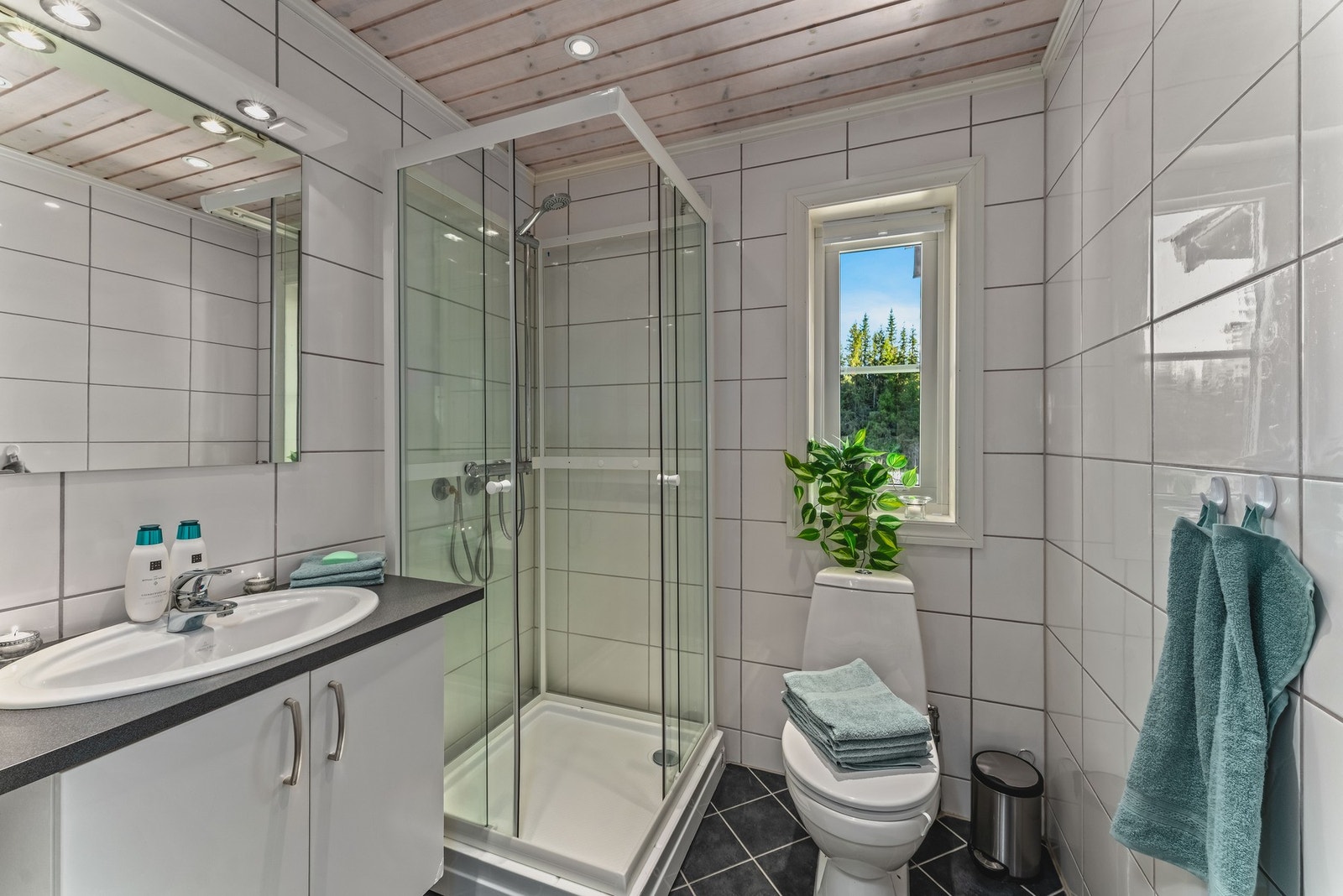 Badet er tidløst innredet med fliser på vegger og gulv, elektrisk gulvvarme, dusjkabinett, servant, toalett og elektrisk vifte. Galleribilde