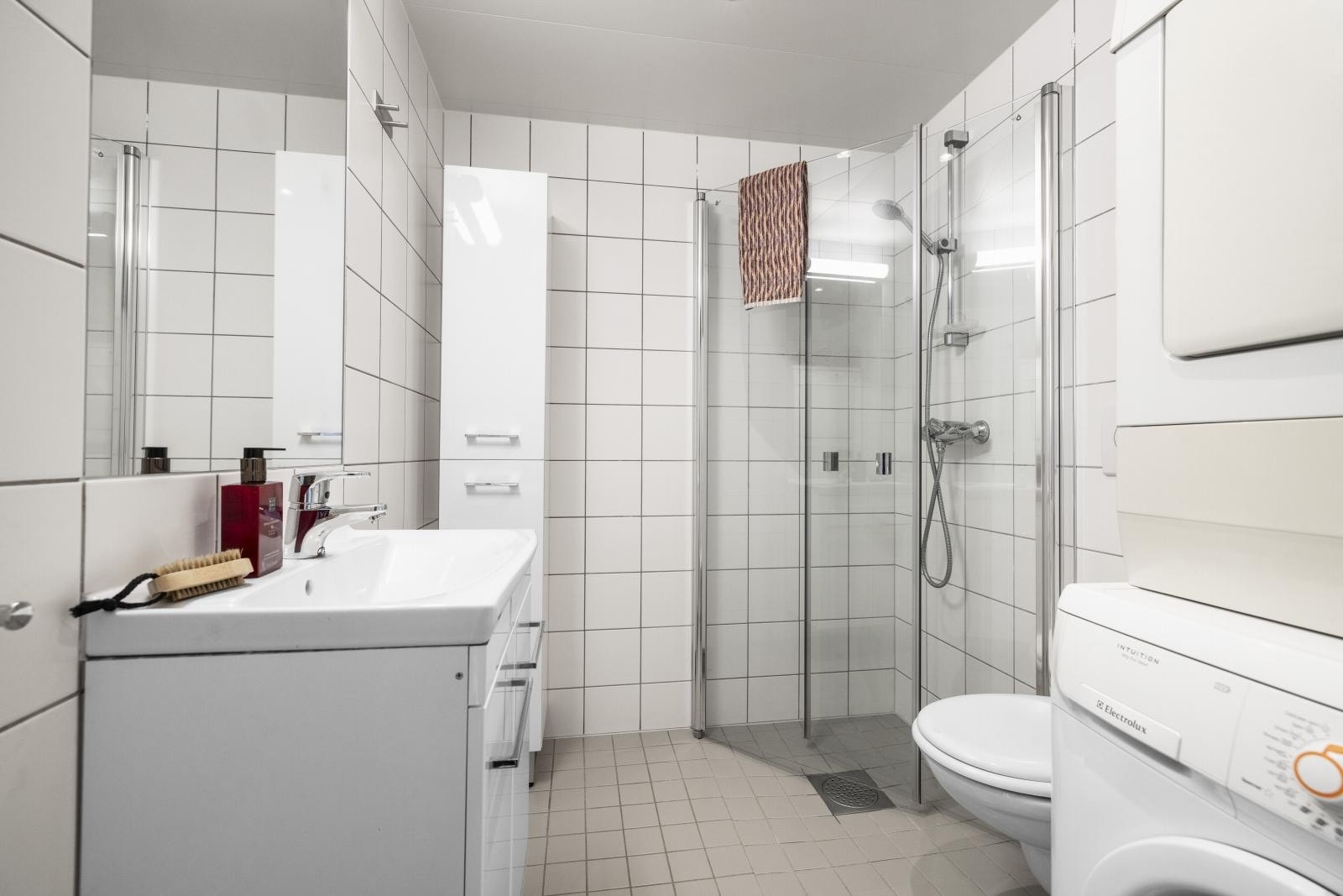 Lyst flislagt bad med opplegg for vaskemaskin og tørketrommel. Vaskemaskin og tørketrommel medfølger salget Galleribilde