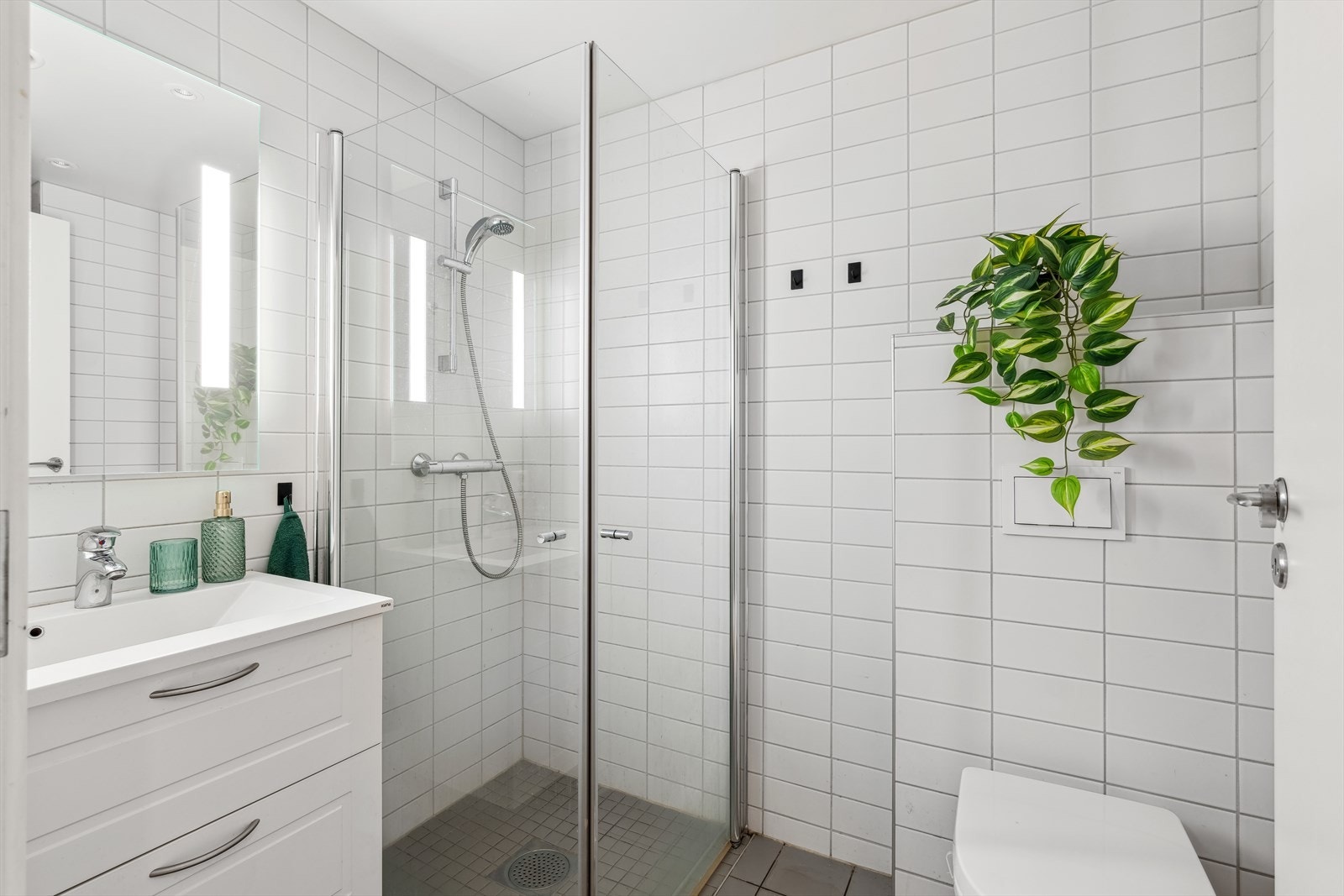 Flislagt bad med servant i skuffinnredning, dusj med glassdører og vegghengt toalett. Galleribilde