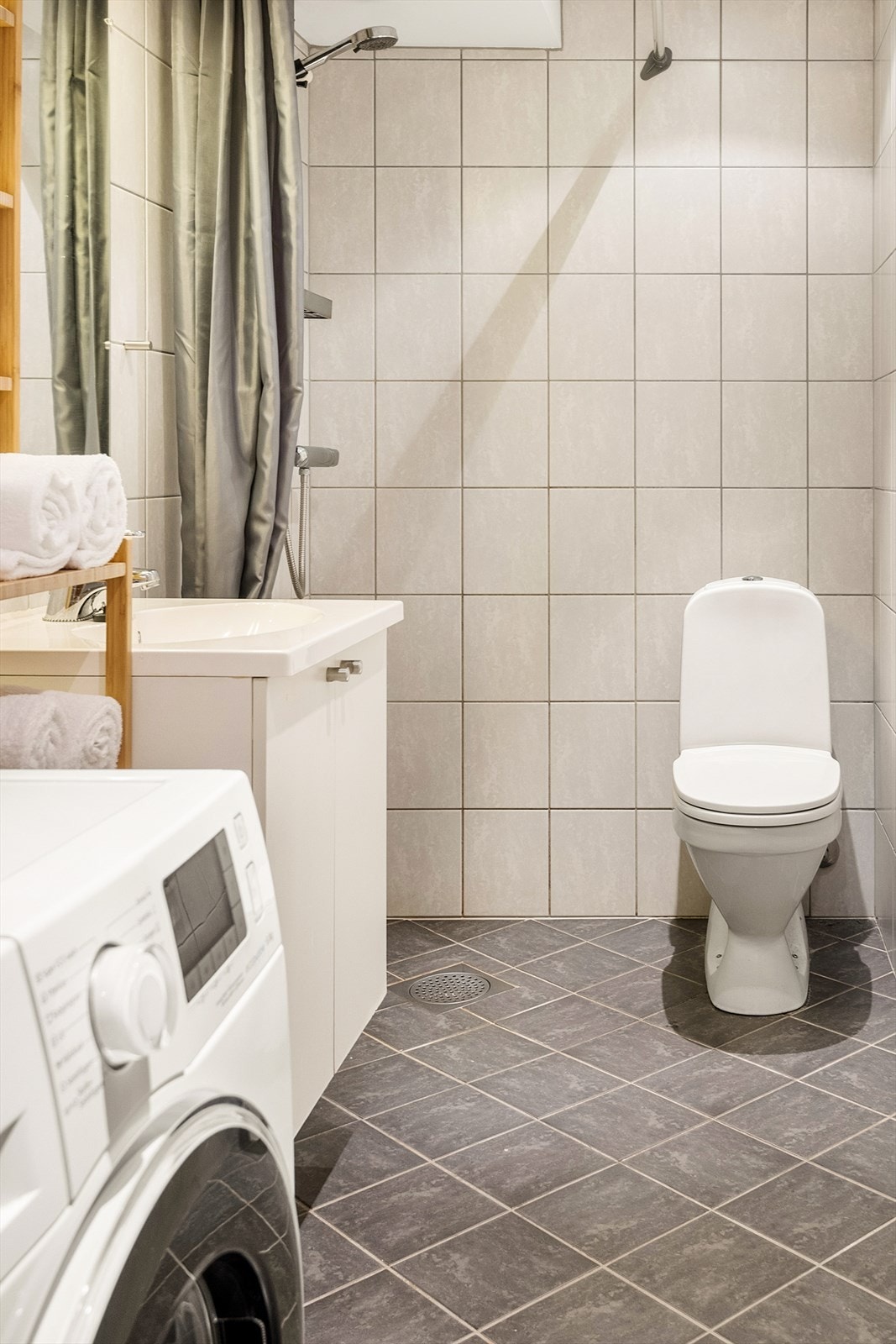 Pent helfliset bad innredet med baderomsinnredning med servant, toalett, dushjørne og opplegg for vaskemaskin. Galleribilde