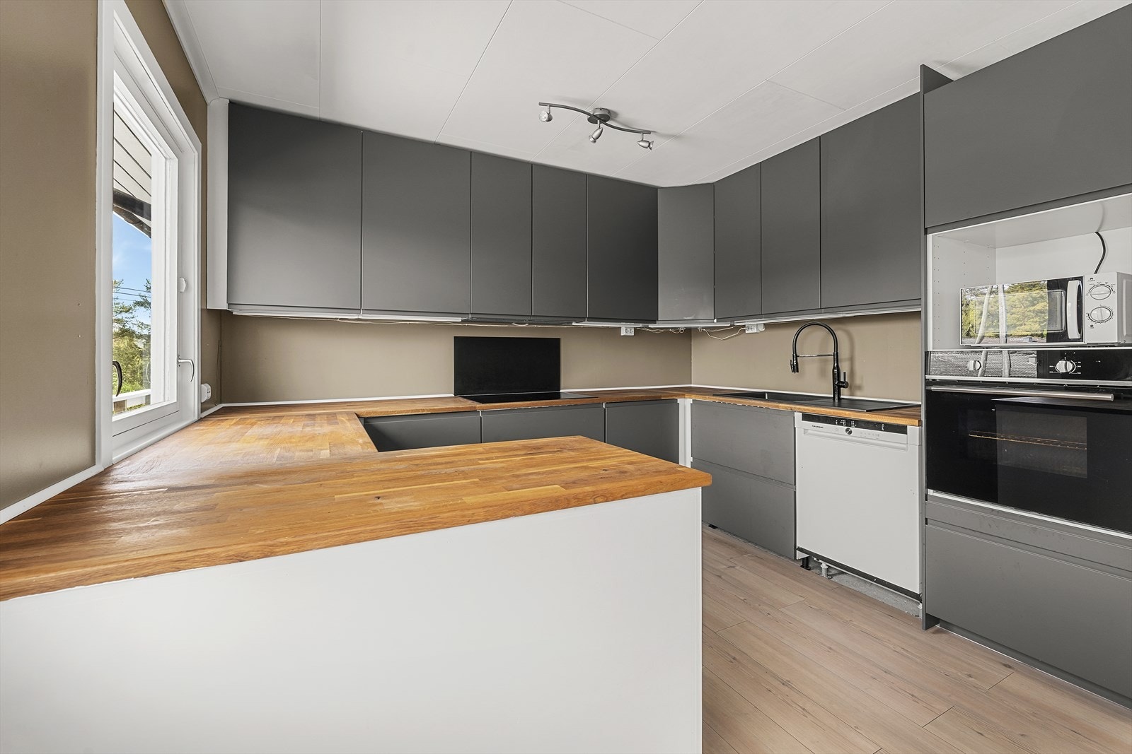 Kjøkkeninnredningen har grå, slette fronter og heltre benkeplate Galleribilde