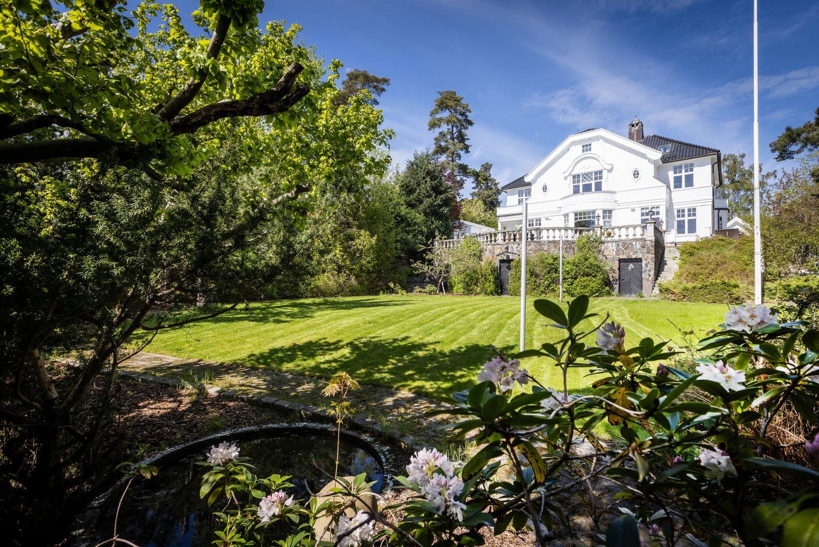 Velstelt og frodig have som omkranser eiendommen med grønne plenområder Galleribilde