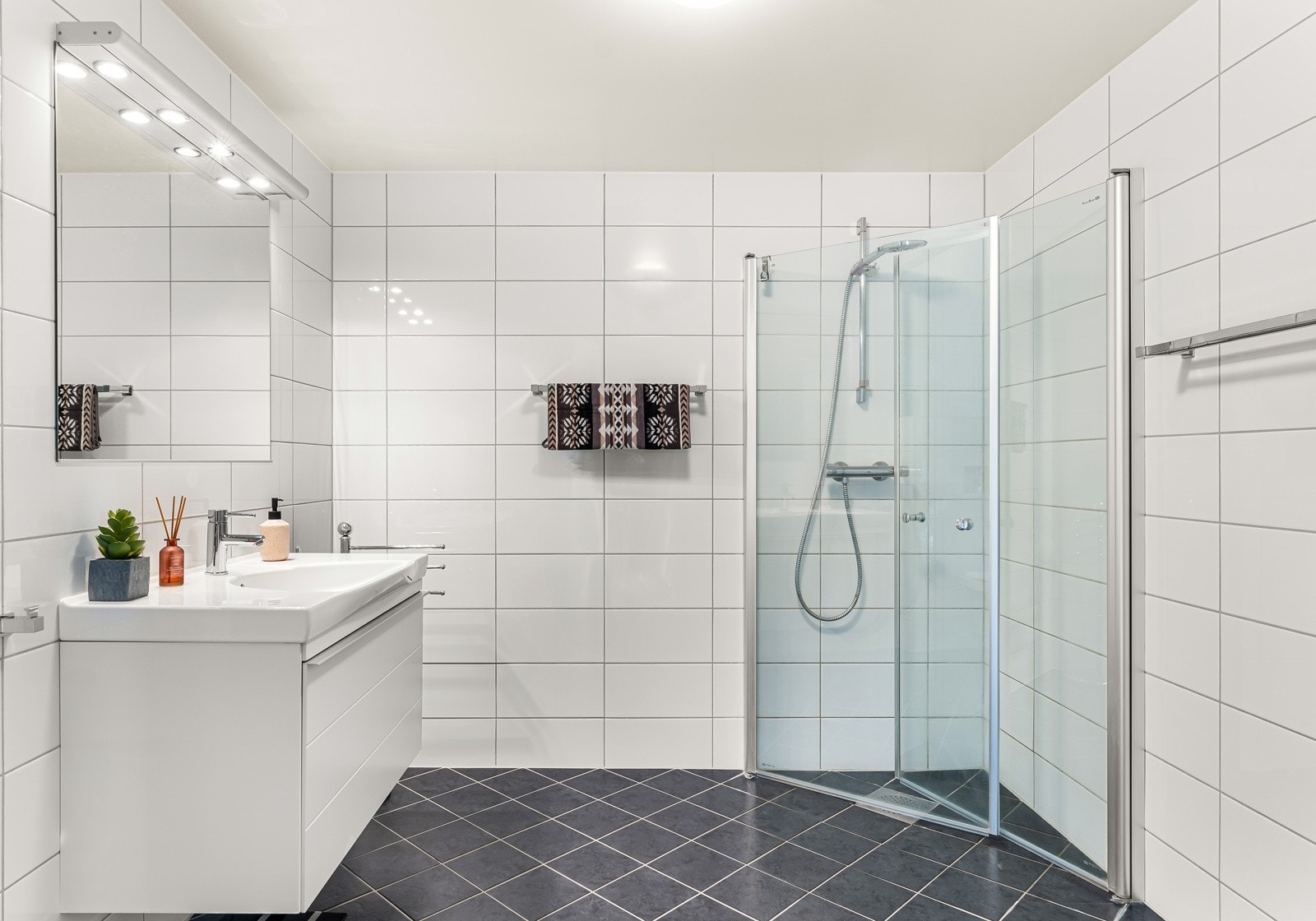 Badet har speil og servantskap, vegghengt-toalett, servant og dusj med glassdører. Det er balansert ventilasjon. Galleribilde