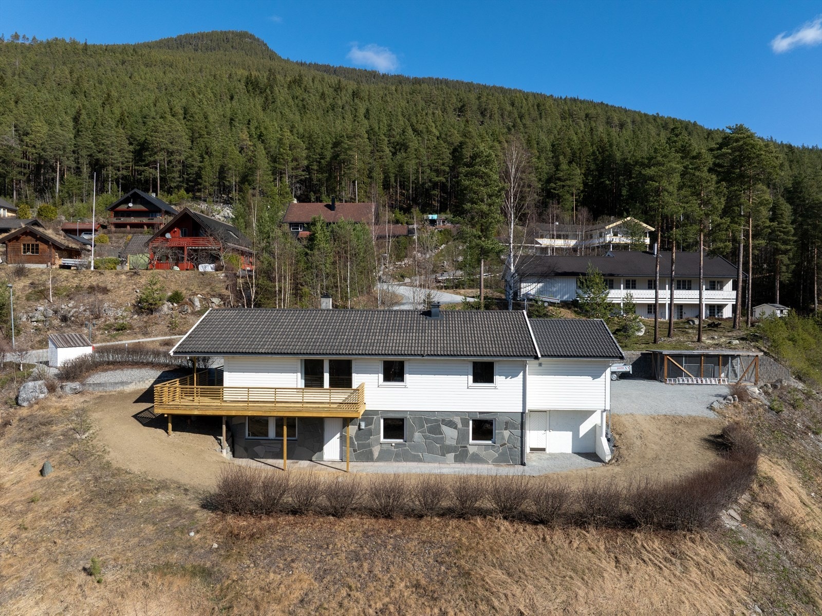 Romslig uteområde, opparbeidet med både plen (nylig sådd), beplantning, støttemur, heller og gruset gårdsplass. Galleribilde